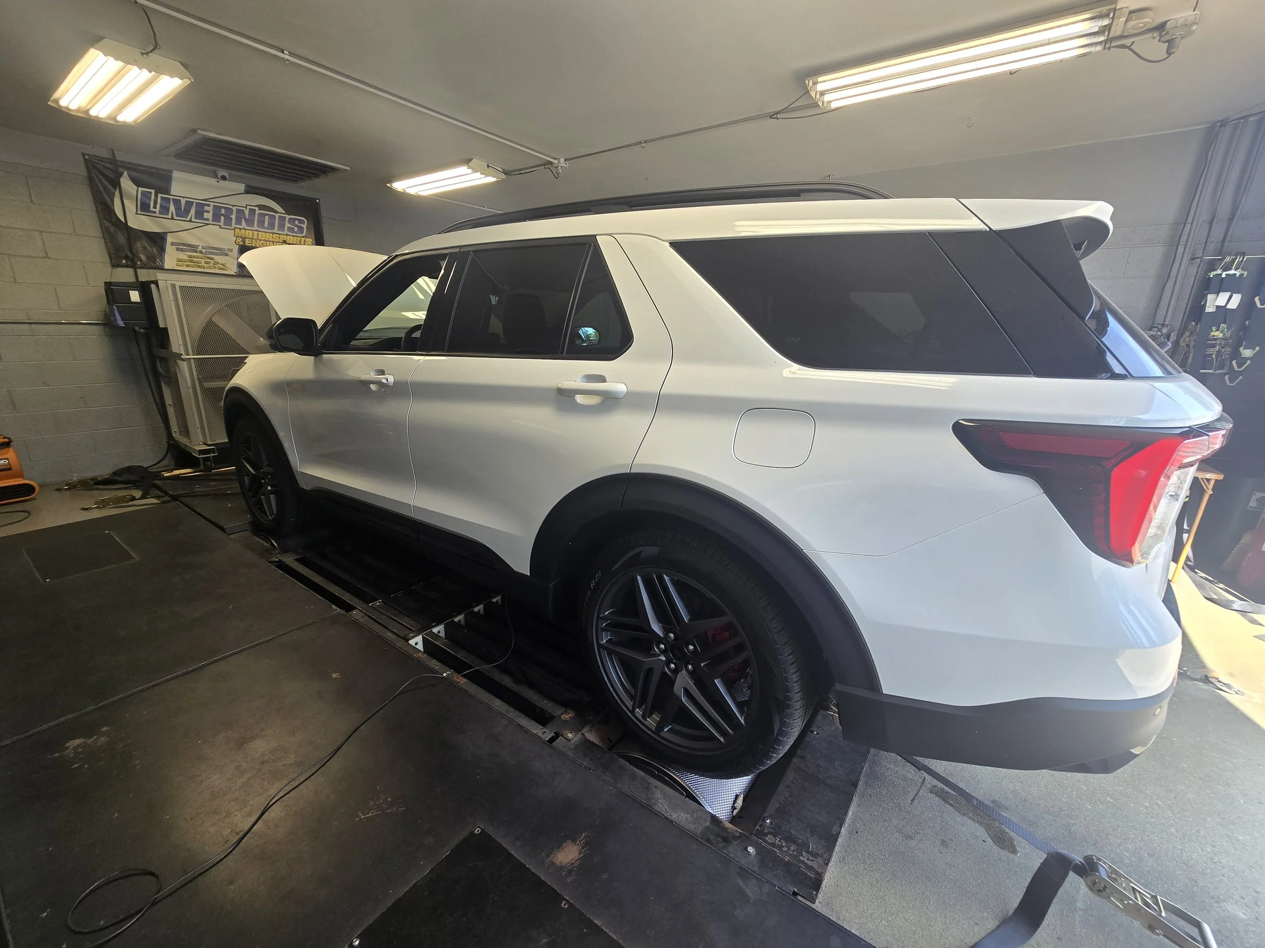 White SUV on a dynamometer inside a garage, with the hood open and a banner reading 'Livernois' on the wall.
