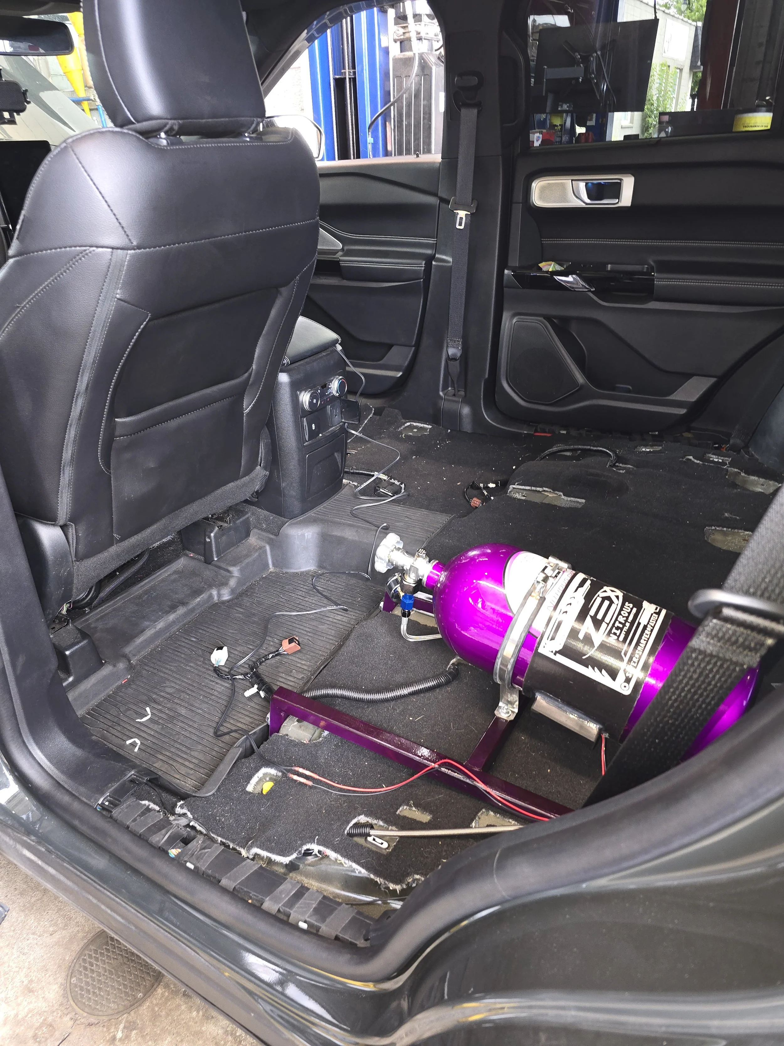 Interior of a Ford Explorer ST with a purple nitrous oxide tank installed in the back seat area, with wires and components visible on the floor.