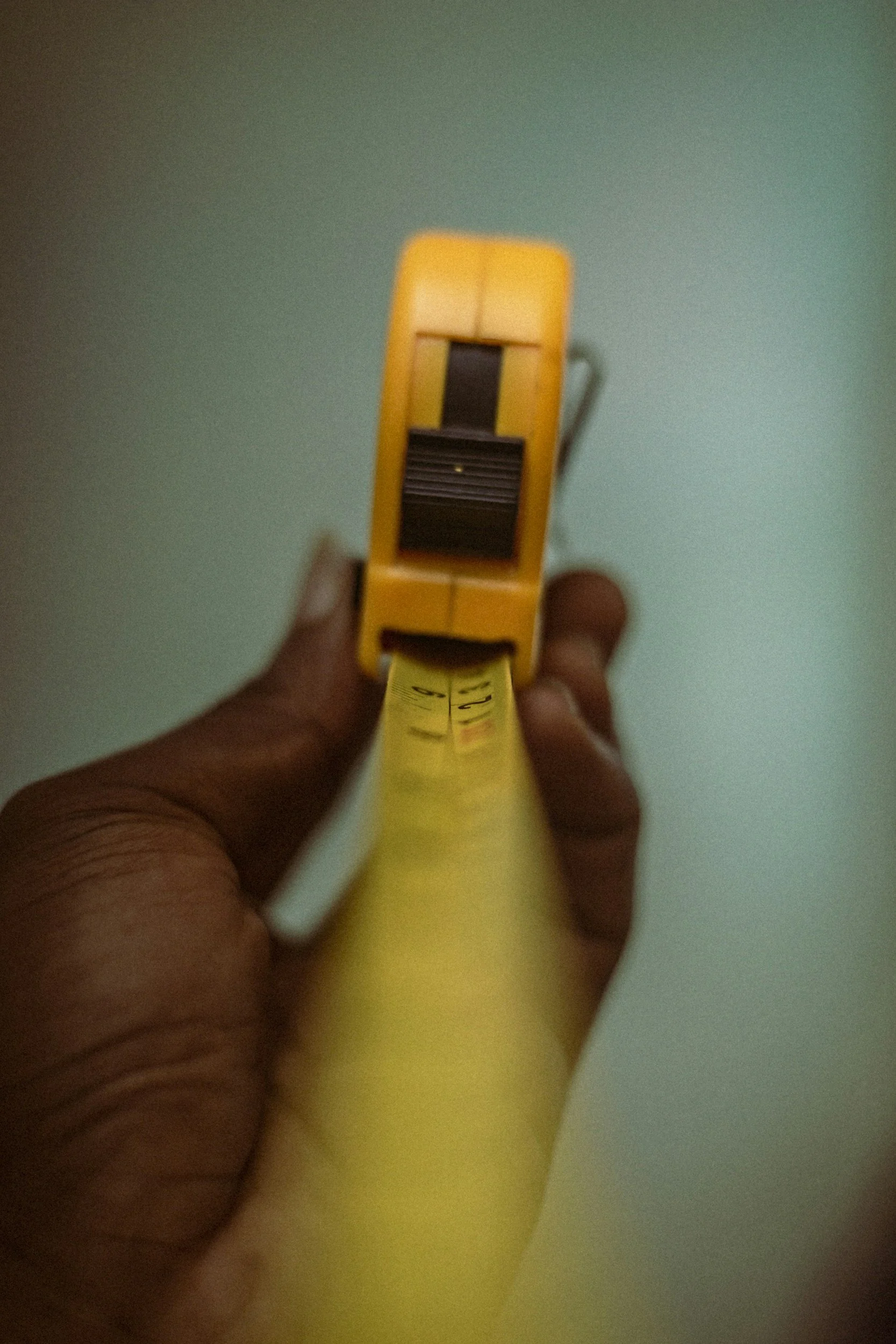 A person holding a yellow box cutter or utility knife, with a black blade mechanism, against a plain background.