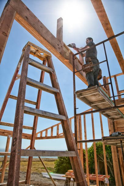 Two construction workers stand on scaffolding, working on building a wooden frame at a construction site under a bright sky.