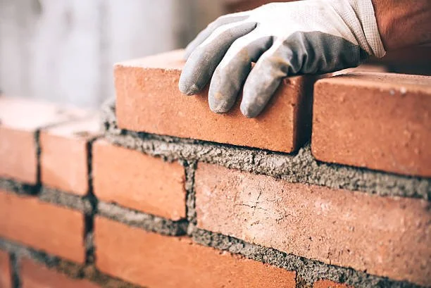 Close-up of a gloved hand laying bricks during construction of a brick wall.