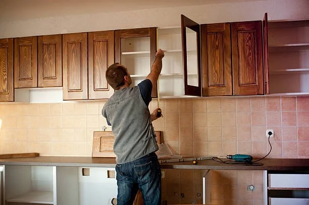 A person installing or adjusting wooden kitchen cabinet doors above a countertop