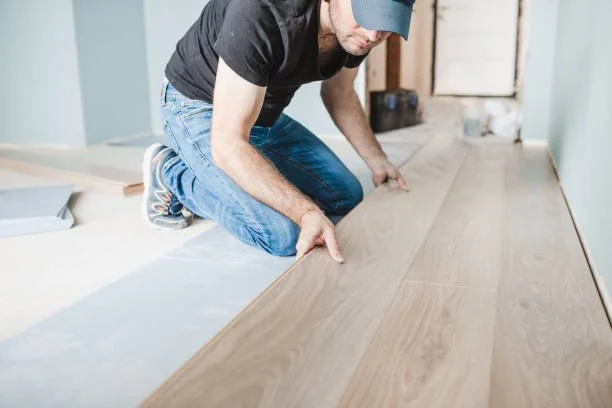 Person installing hardwood flooring in a room.