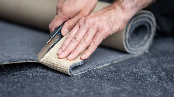 A person cutting carpet with scissors while unrolling a carpet roll.