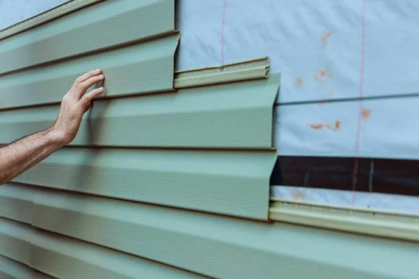 Close-up of someone installing green siding on a building under construction.