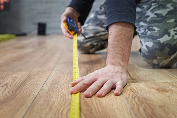 Person measuring a wooden floor with a yellow tape measure.