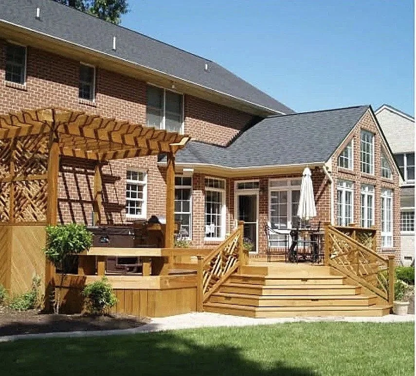 by Custom Design Works Inc. Hampton Roads construction contractor | Wooden deck with stairs, outdoor dining table with chairs, grill, a garden with plants, and a brick house with large windows in the background.