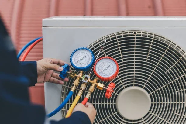 Technician's hands adjusting HVAC refrigerant gauges on an air conditioning unit.