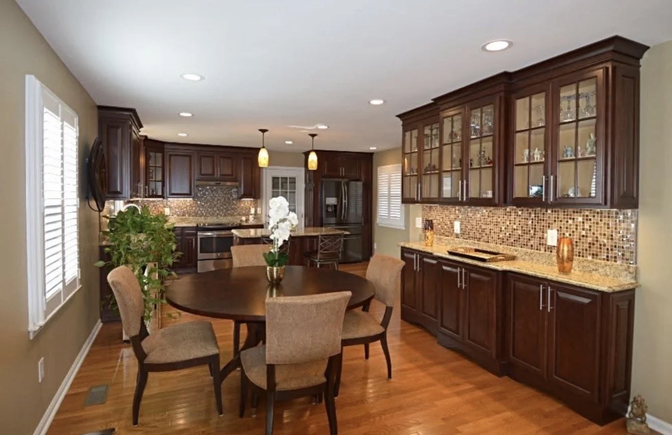 by Custom Design Works Inc. Hampton Roads construction contractor | A kitchen with dark wood cabinets, a dining table with chairs, and a mosaic tile backsplash.
