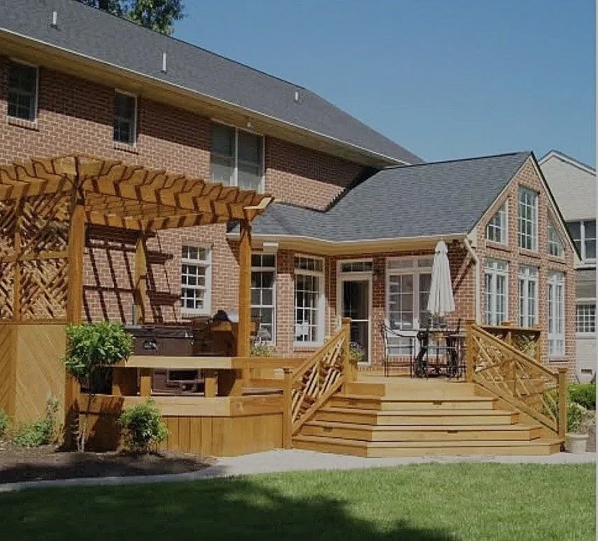 by Custom Design Works Inc. Hampton Roads construction contractor | Backyard with wooden deck and patio furniture, house with large windows, brick exterior, and gabled roof.
