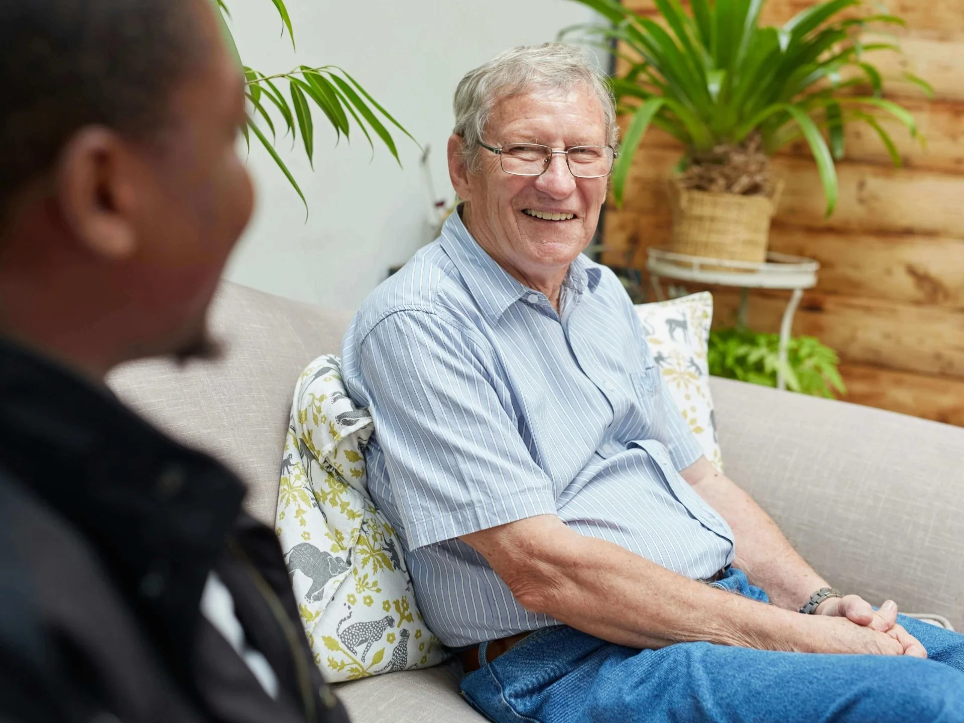 Happy elderly man in home on couch with residential health service employee.