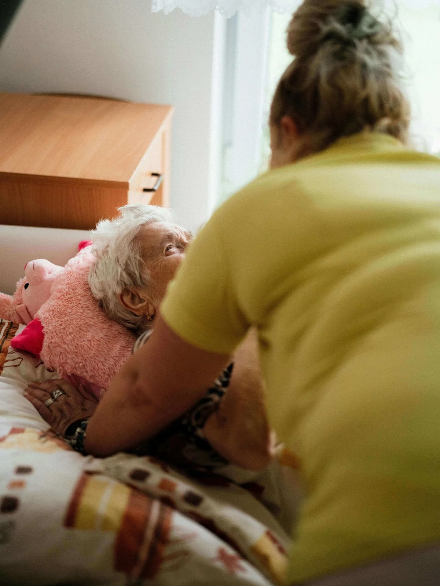 In home personal care worker leaning over elderly customer lying in bed.