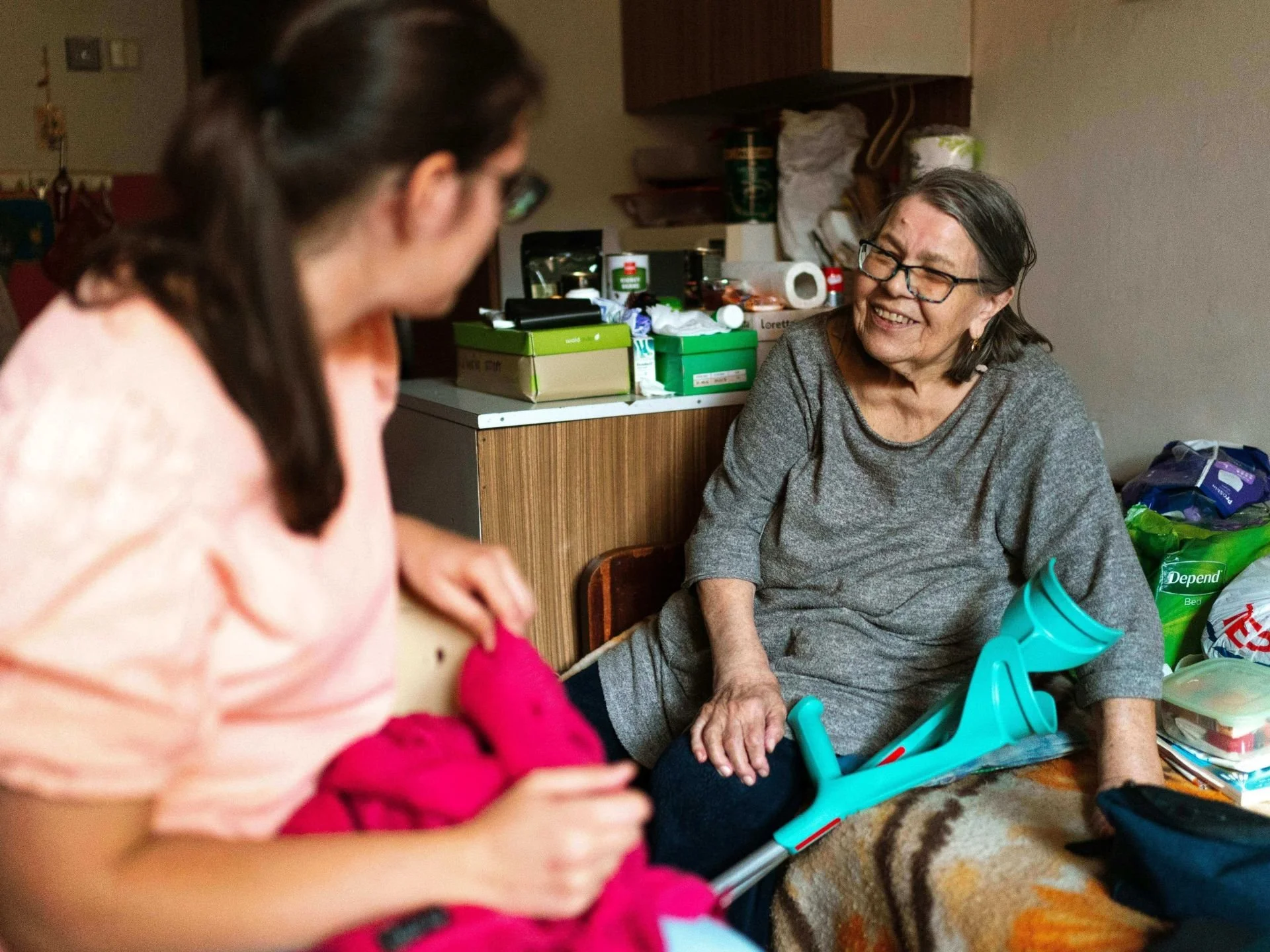 Elderly disabled woman with crutches smiling talking to CNA caregiver in home in Kansas City.