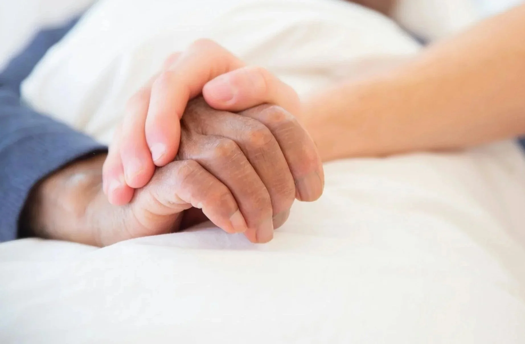Hand of healthcare worker on top of elderly hand on bedsheets in Kansas City home.