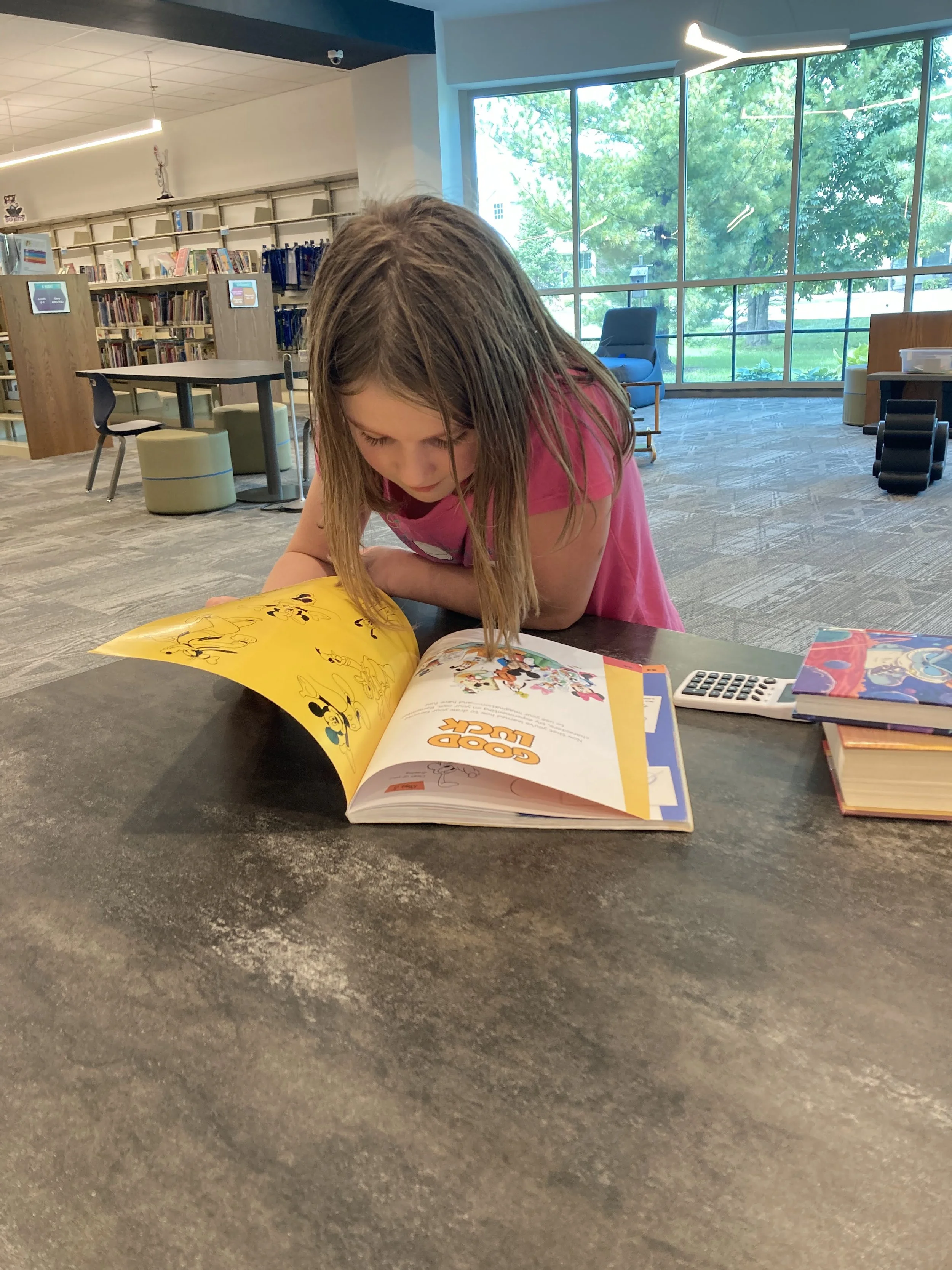 A young girl with long hair reading a comic book in a library