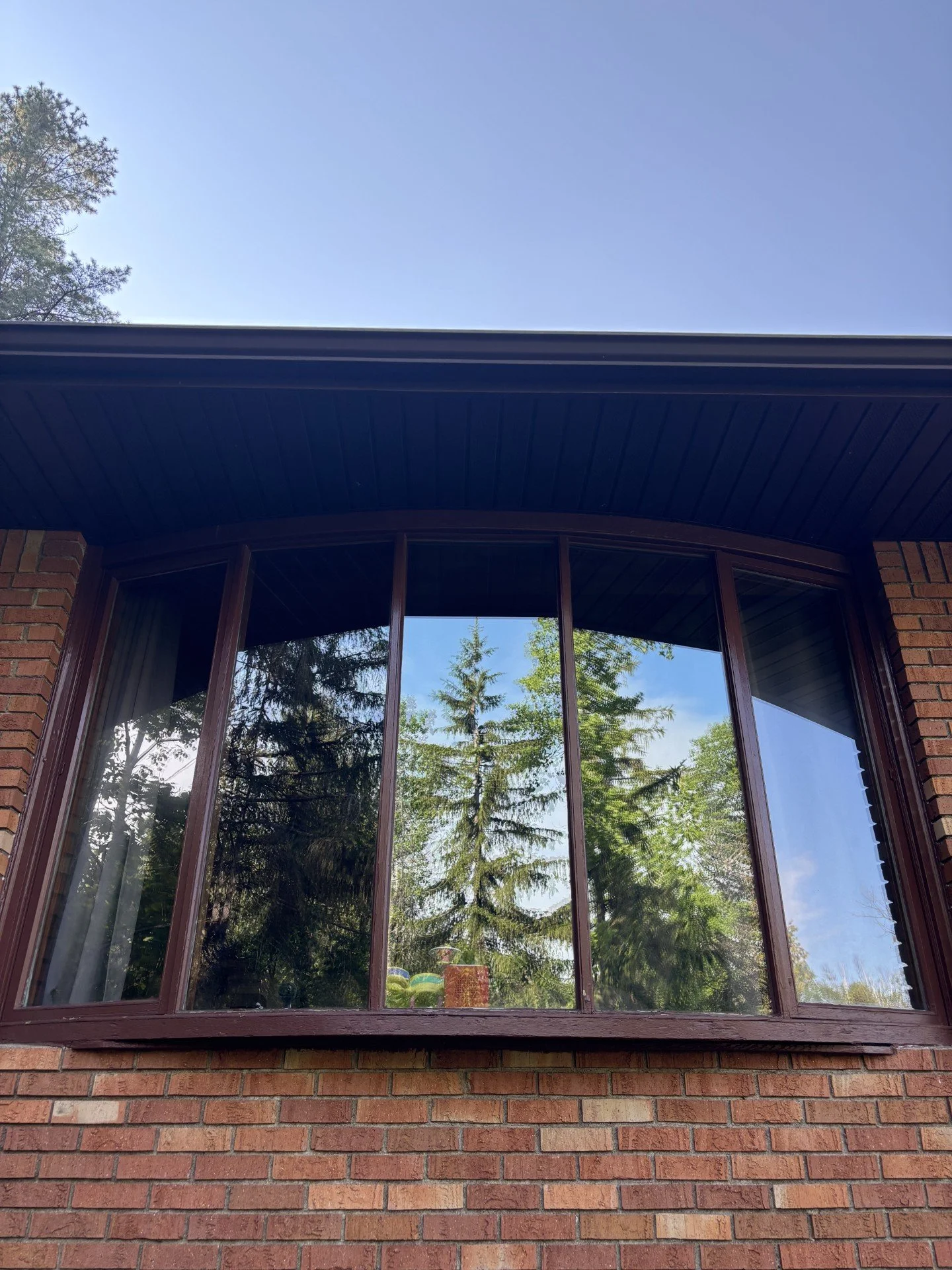 View of a large brick house window with trees and blue sky reflected in the glass.