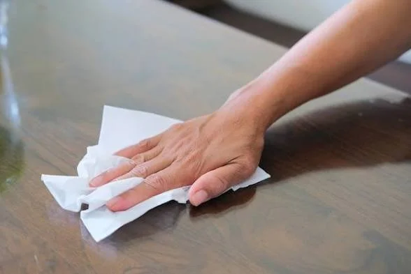 Hand wiping a wooden surface with a white cloth.