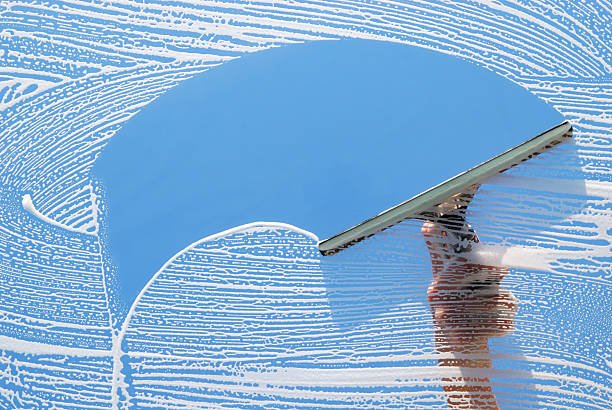A person cleaning a large glass window with a squeegee, leaving streaks behind.