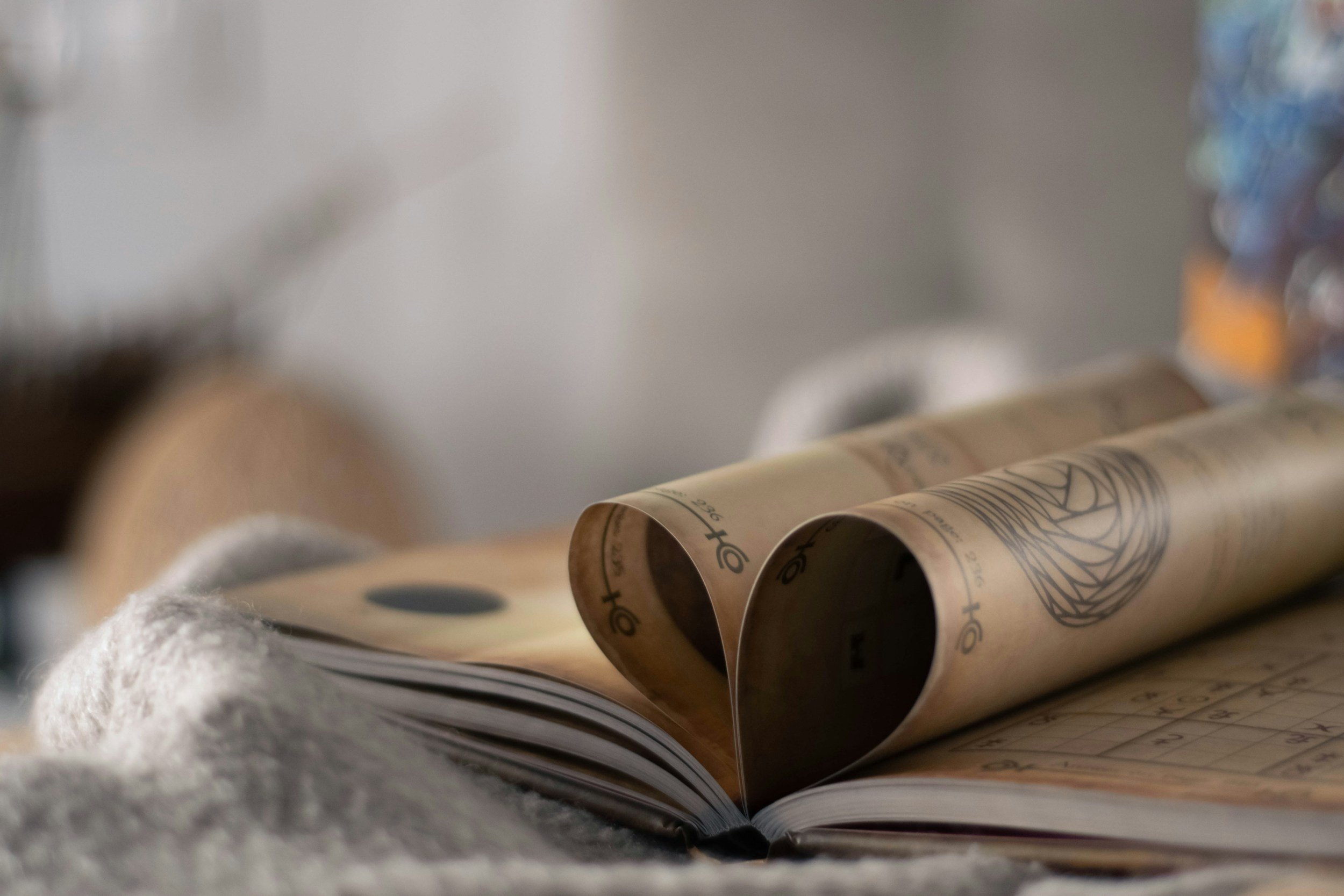 A book with pages rolled into a heart, placed on a textured surface, with a blurred background.
