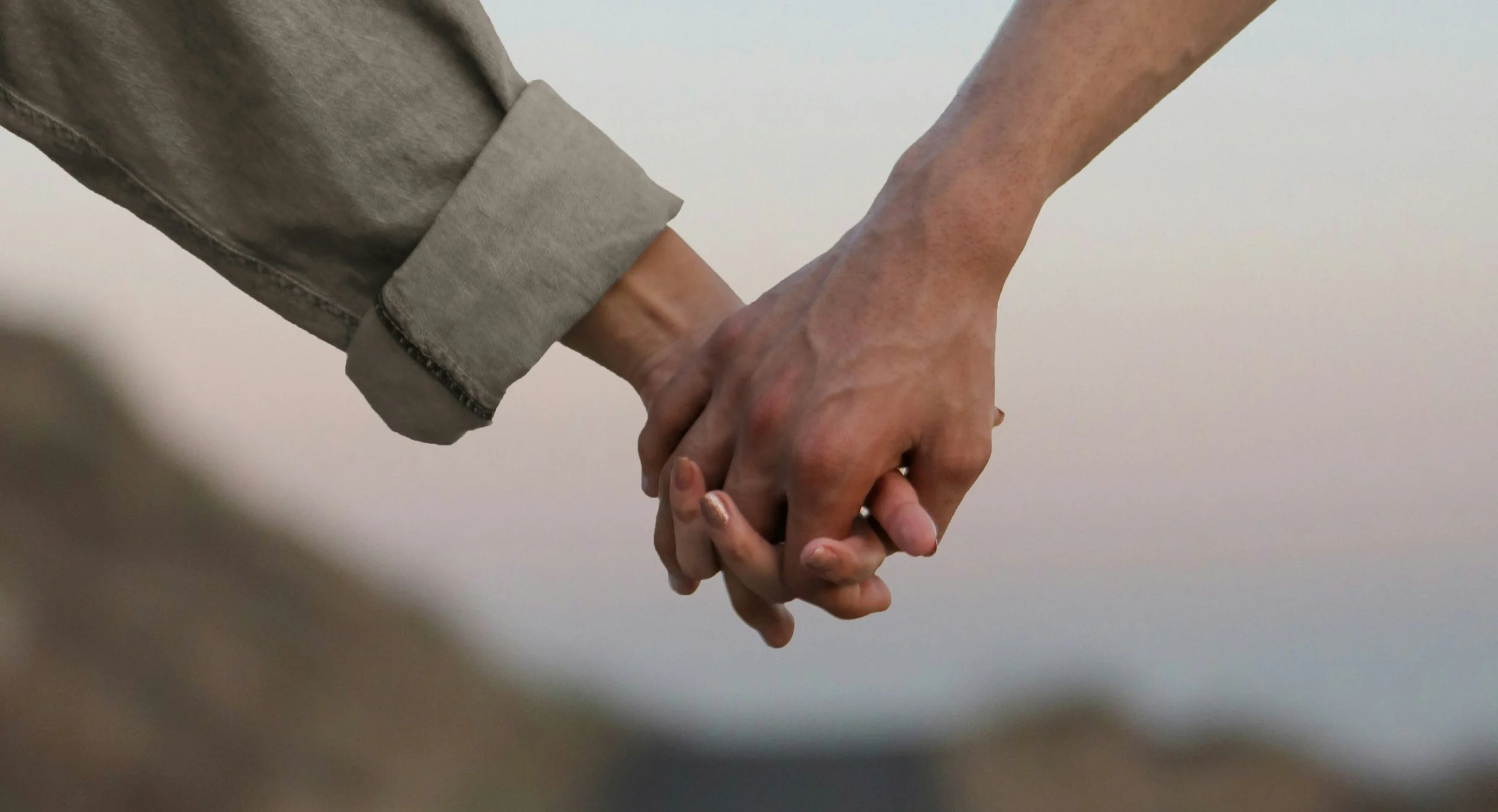 Close-up of two people holding hands, one person wearing a light-colored jacket and the other with natural skin tone.