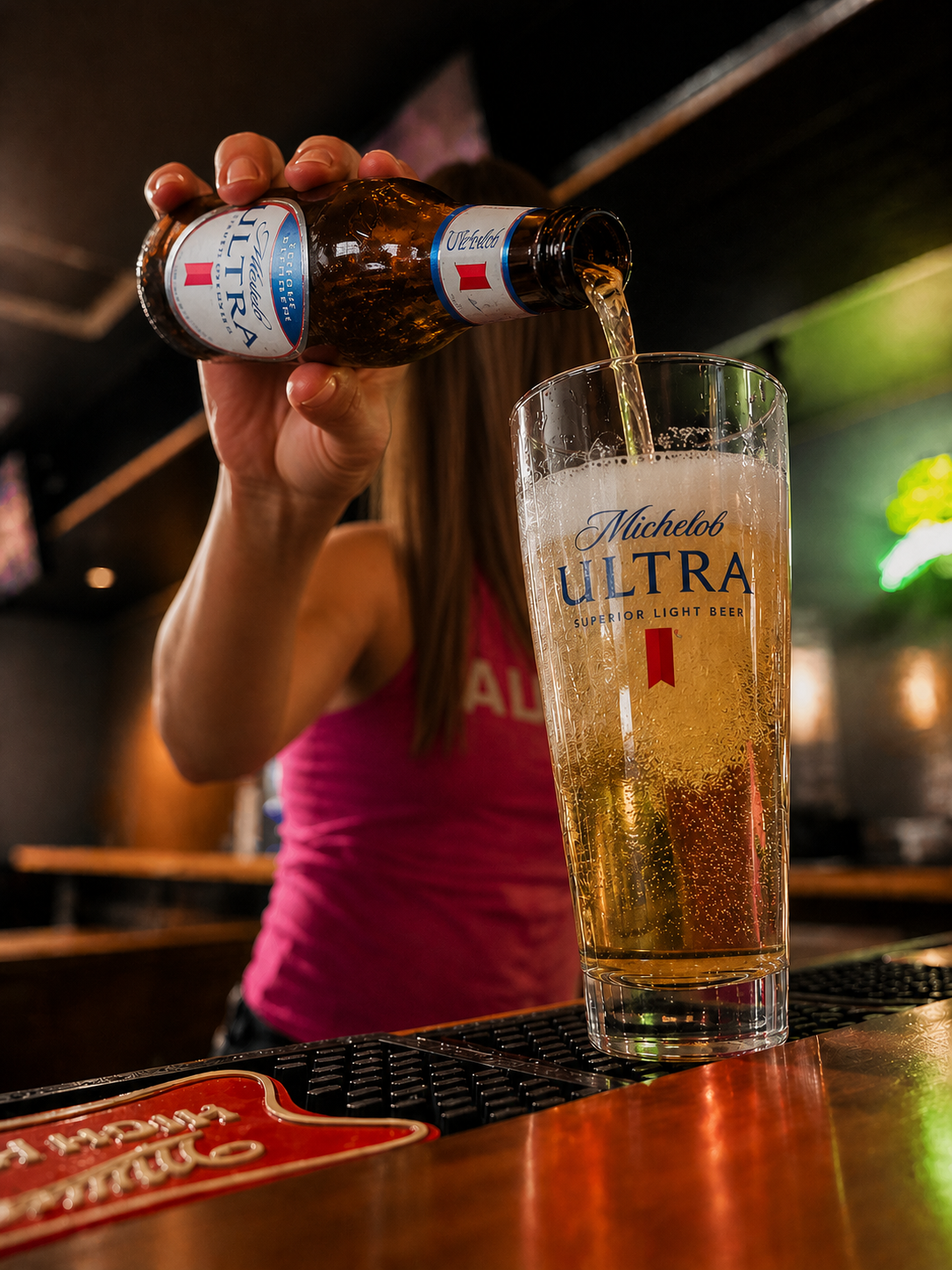 Person pouring Michelob Ultra beer into a glass at a bar.