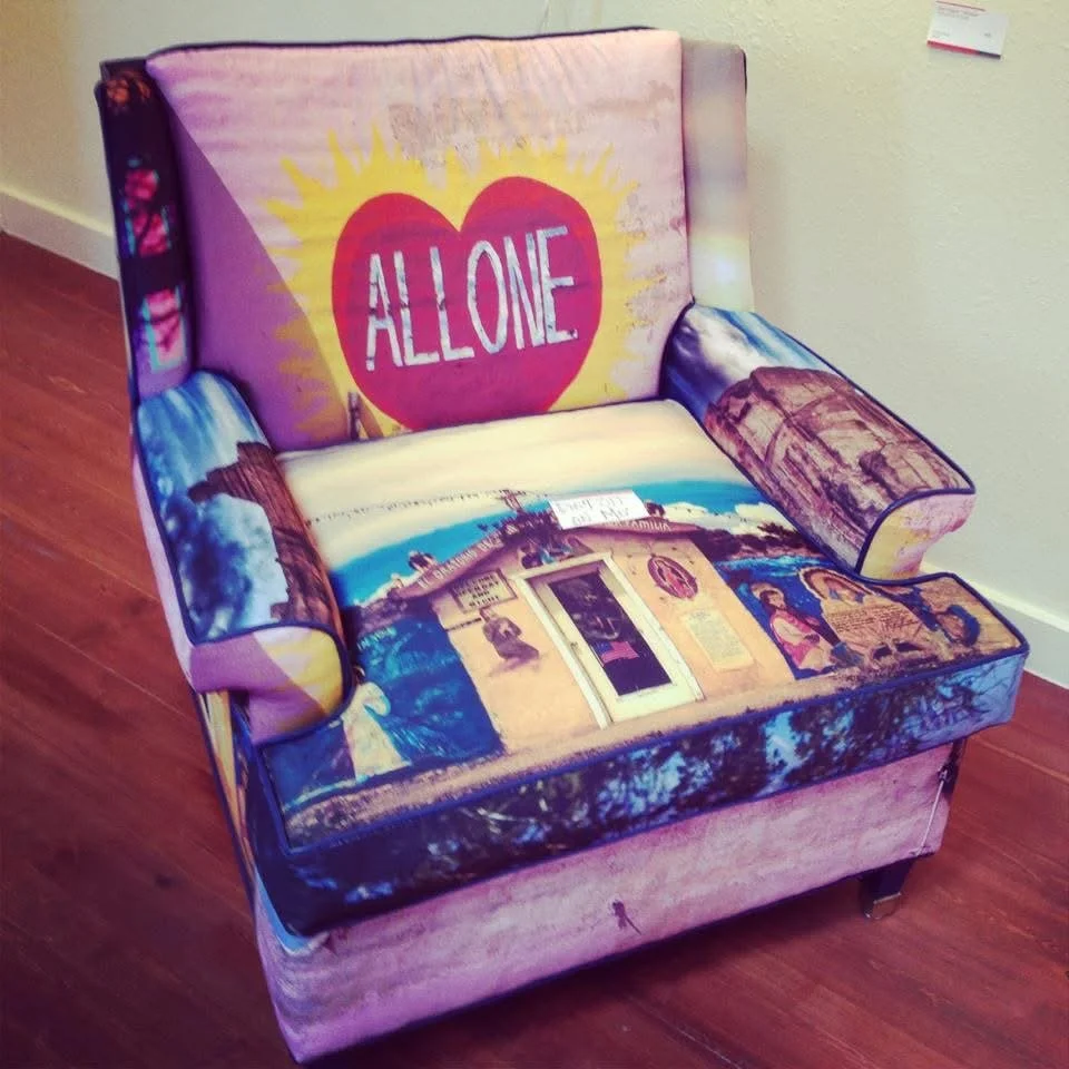 A colorful armchair images and text, including a large heart with the word "ALLONE" on the backrest, and scenic pictures on the seat and armrests. Photograph by Rod Mikinski printed on fabric and reupholstered by Phyllis J Garibay-Coon.