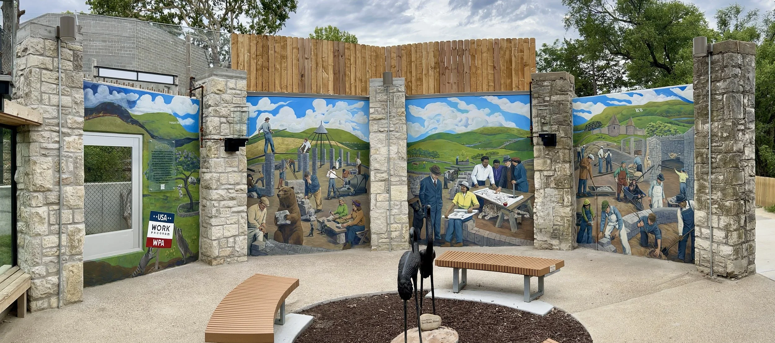 Mural depicting the WPA project that helped build the Sunset Zoo in Manhattan, KS. It showcases scenes of construction workers and zoo animals working together to build the zoo set against rolling green hills if the tall grass prairie.