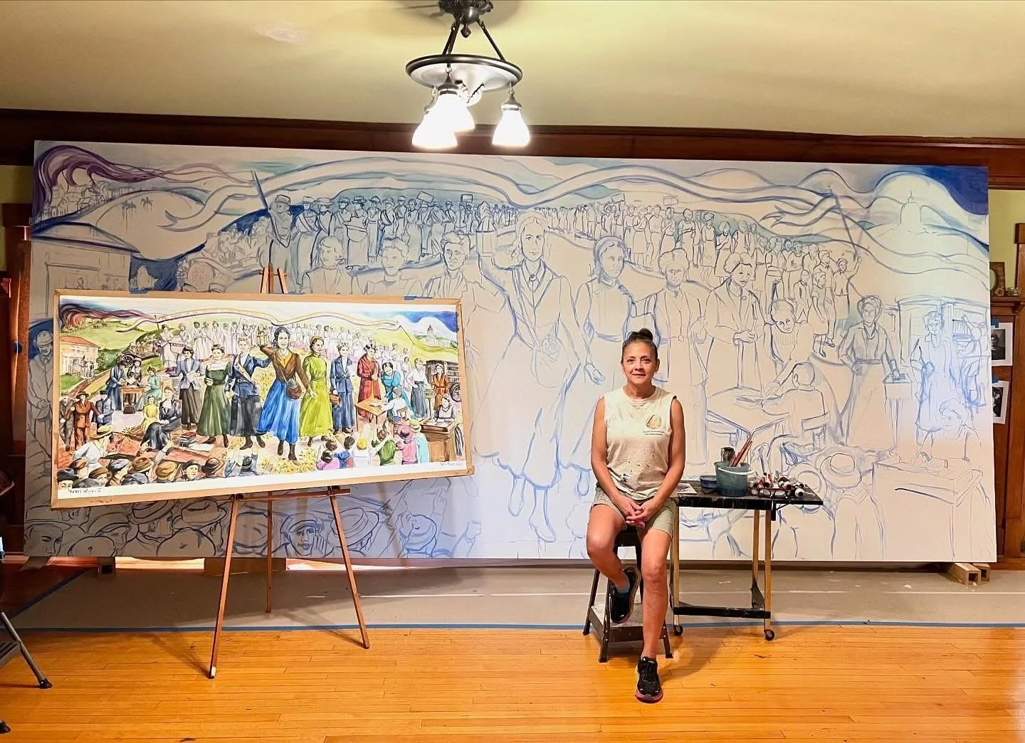 Phyllis J Garibay-Coon sitting in front of her painting "Rebel Women".
