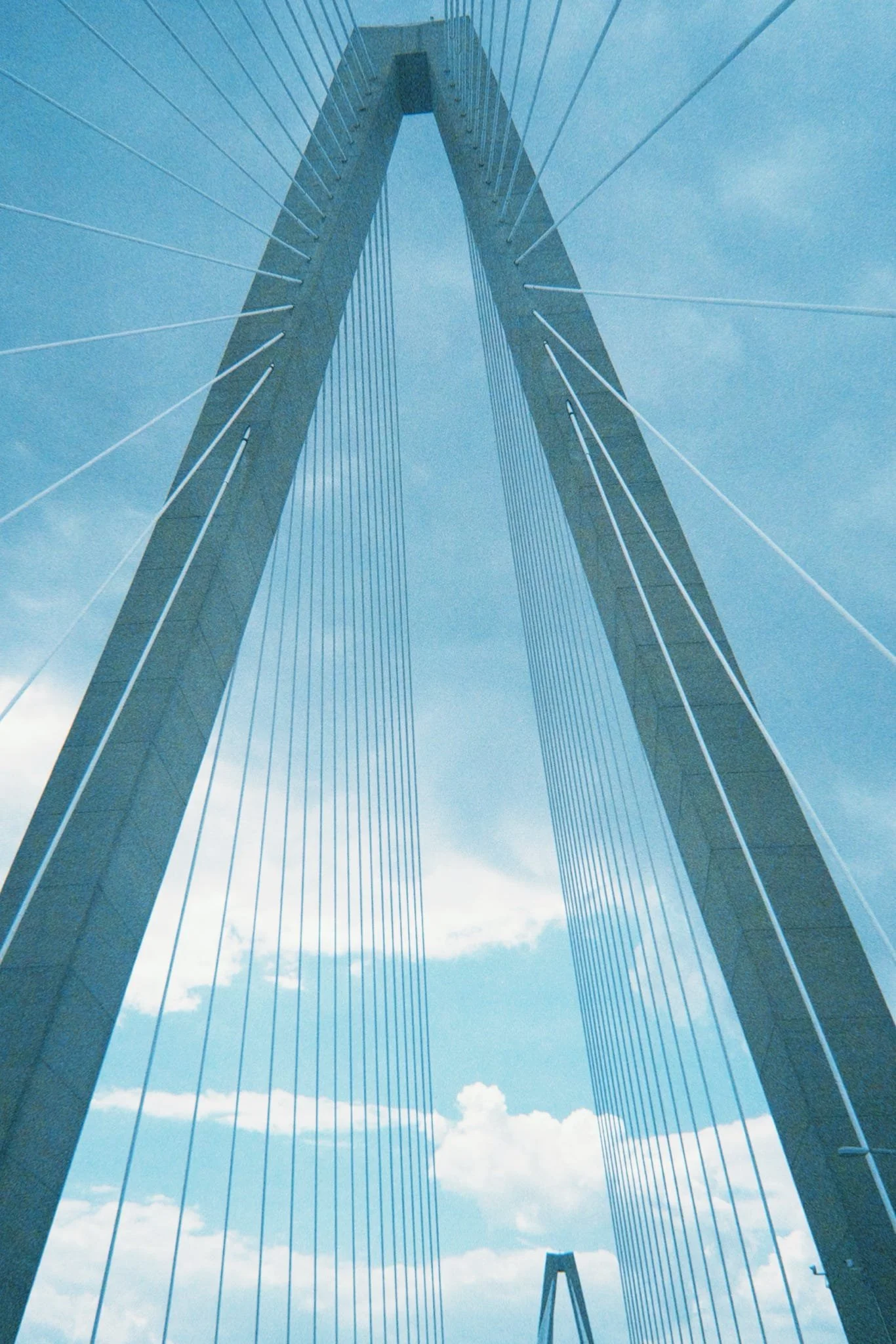 Low-angle view of a modern cable-stayed bridge with a tall, arching central support against a partly cloudy sky.