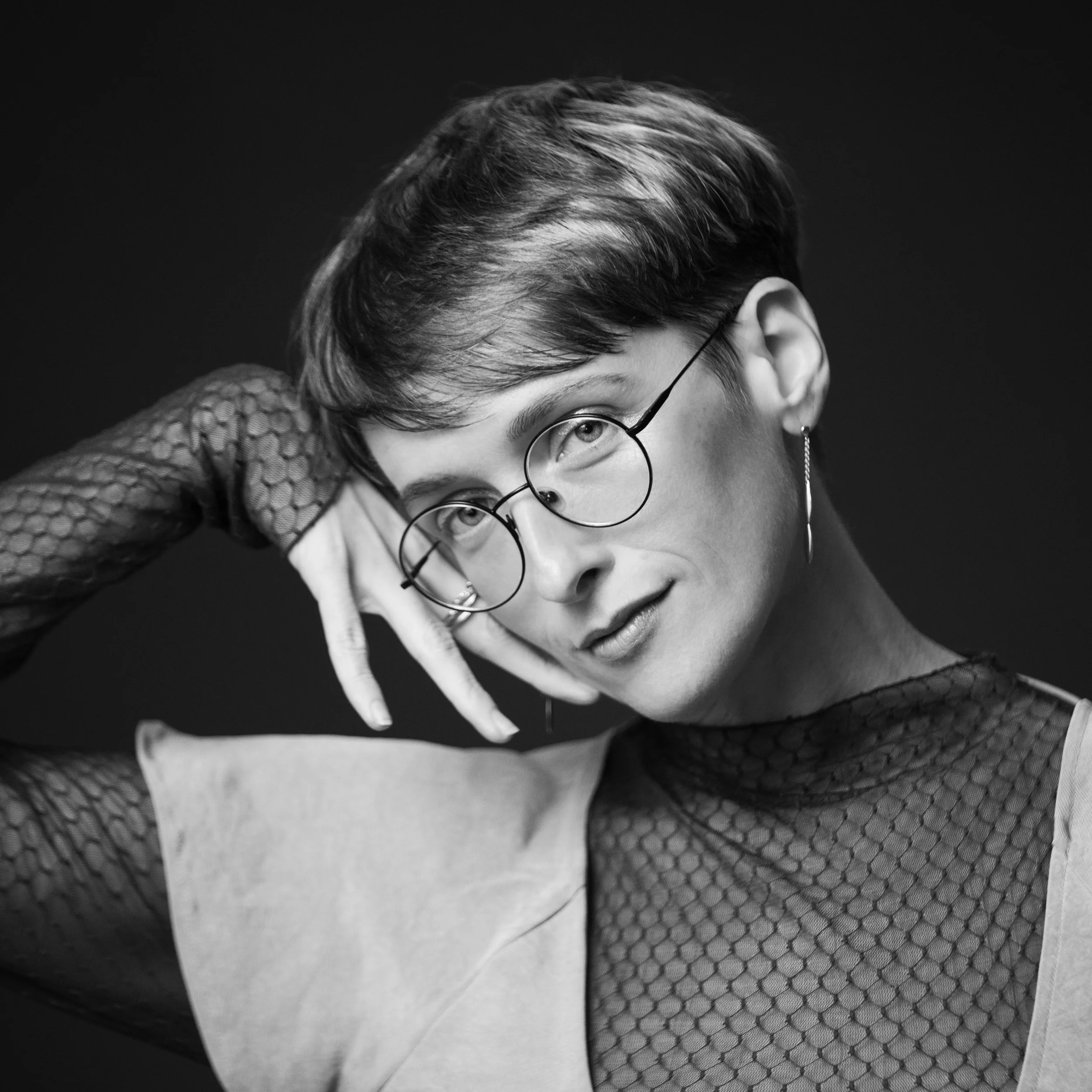Close-up black and white portrait of a woman with short hair and glasses, wearing a textured top.