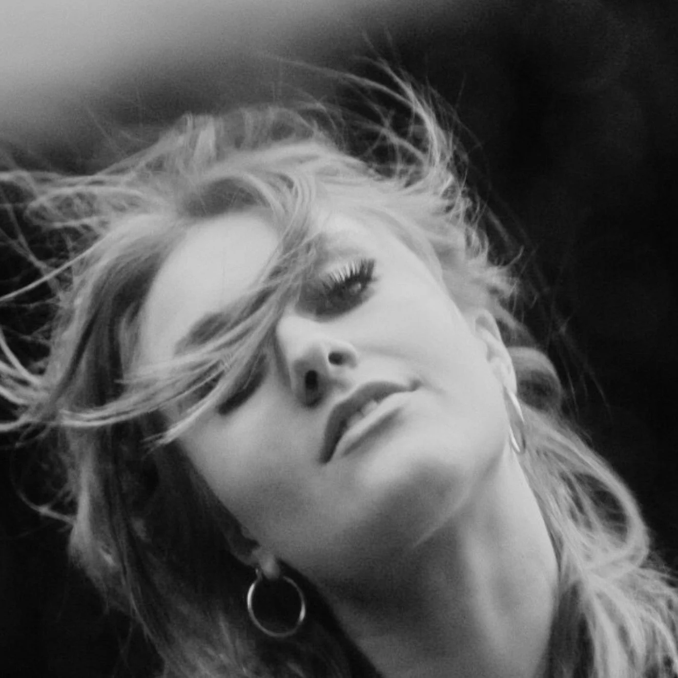 Black and white portrait of a woman with wavy hair partially covering her face, wearing hoop earrings.