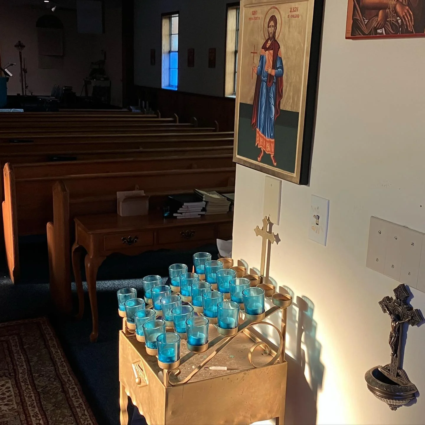 Votive candles sit below the icon of Saint Alban, the proto-martyr of the British Isles. A small holy water font with a crucifix is hung beside the candles.