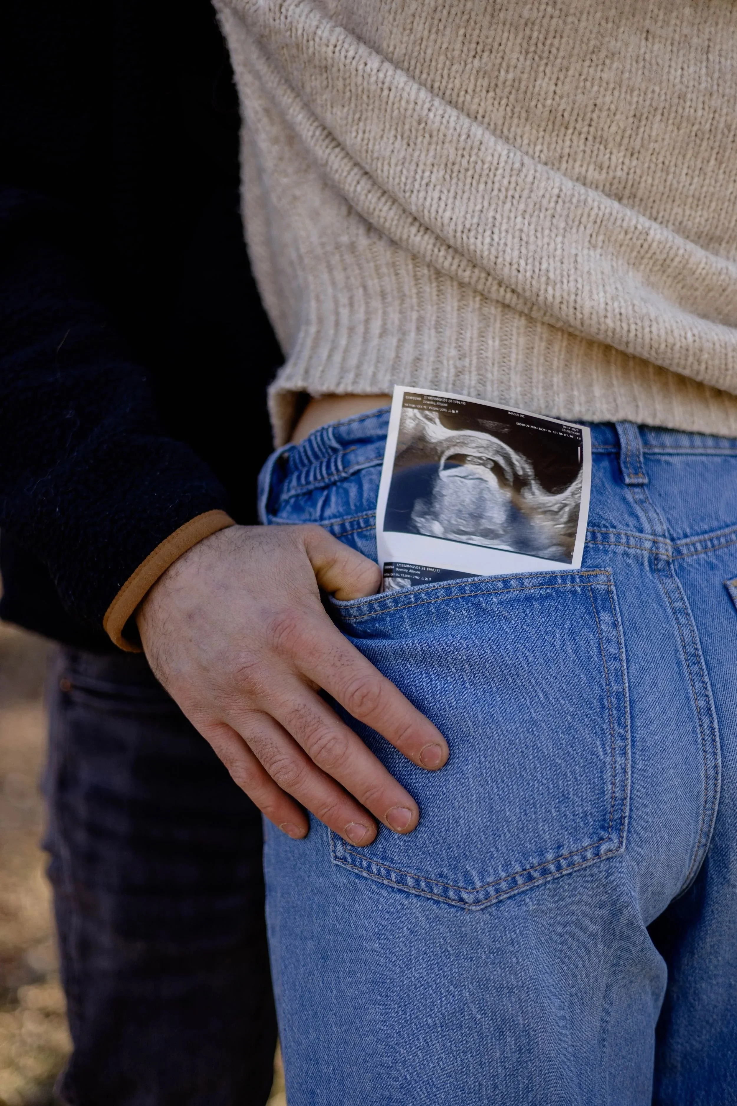 Person holding ultrasound image in back pocket of blue jeans, standing outdoors.
