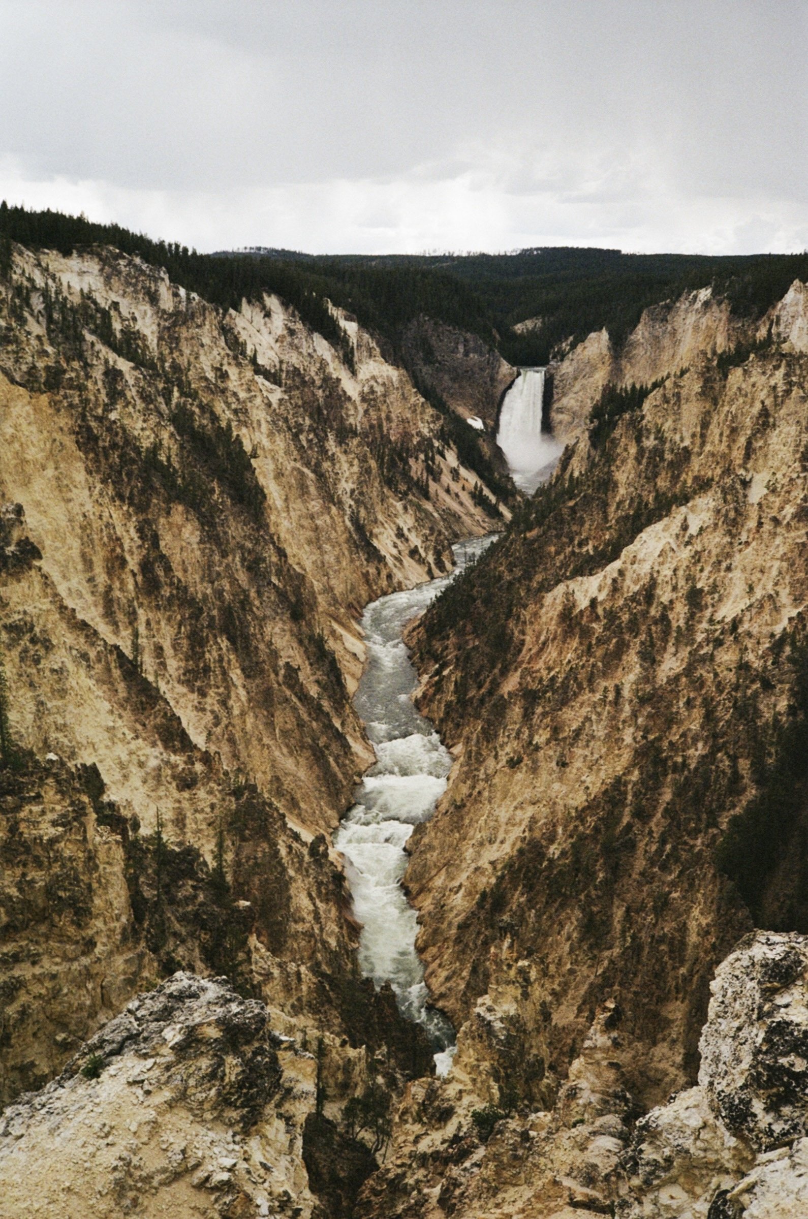 A view of the Grand Canyon with a river and a waterfall in the distance on a cloudy day.