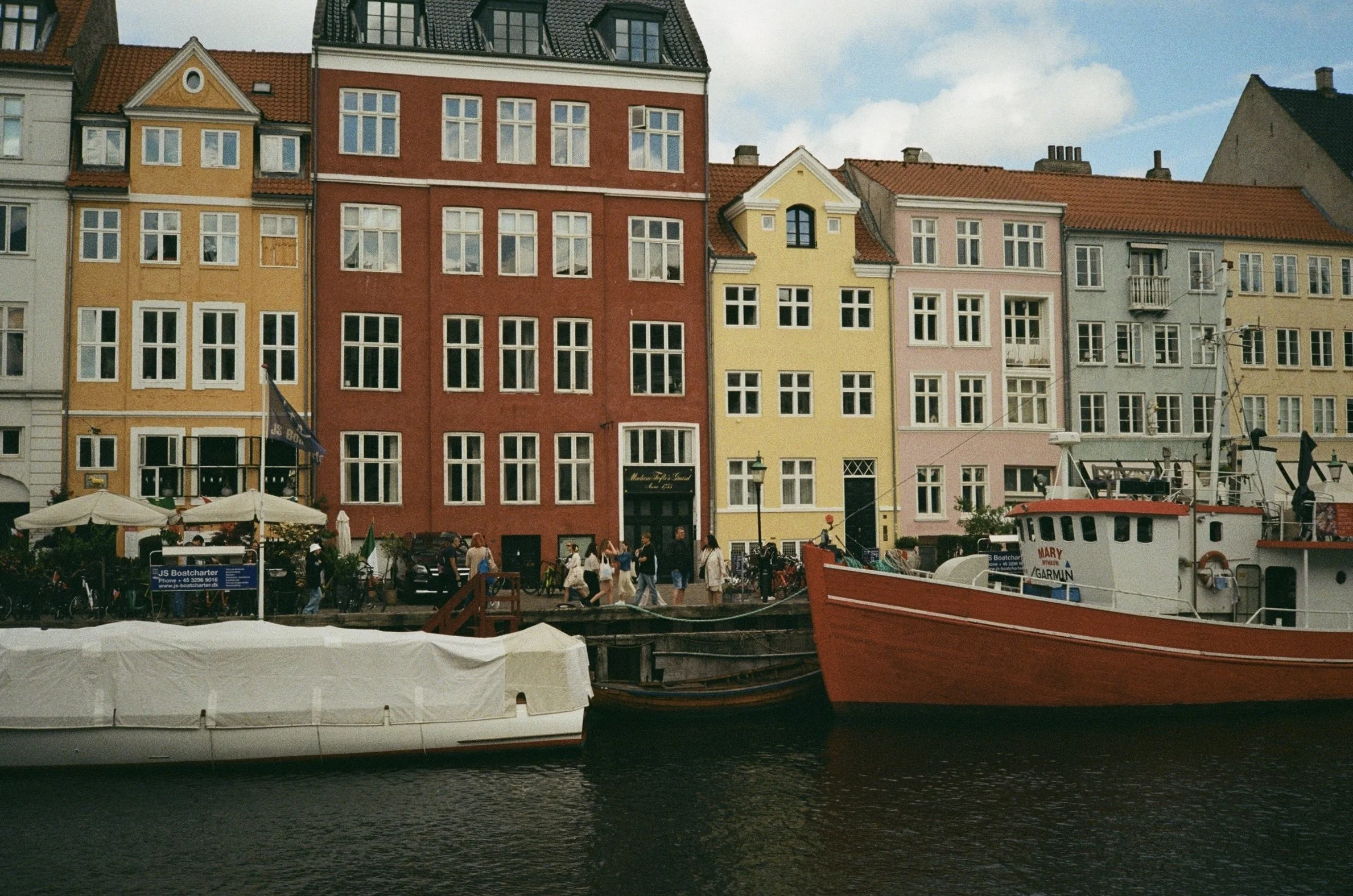 Colorful European buildings along a waterfront with boats and people walking on the dock.
