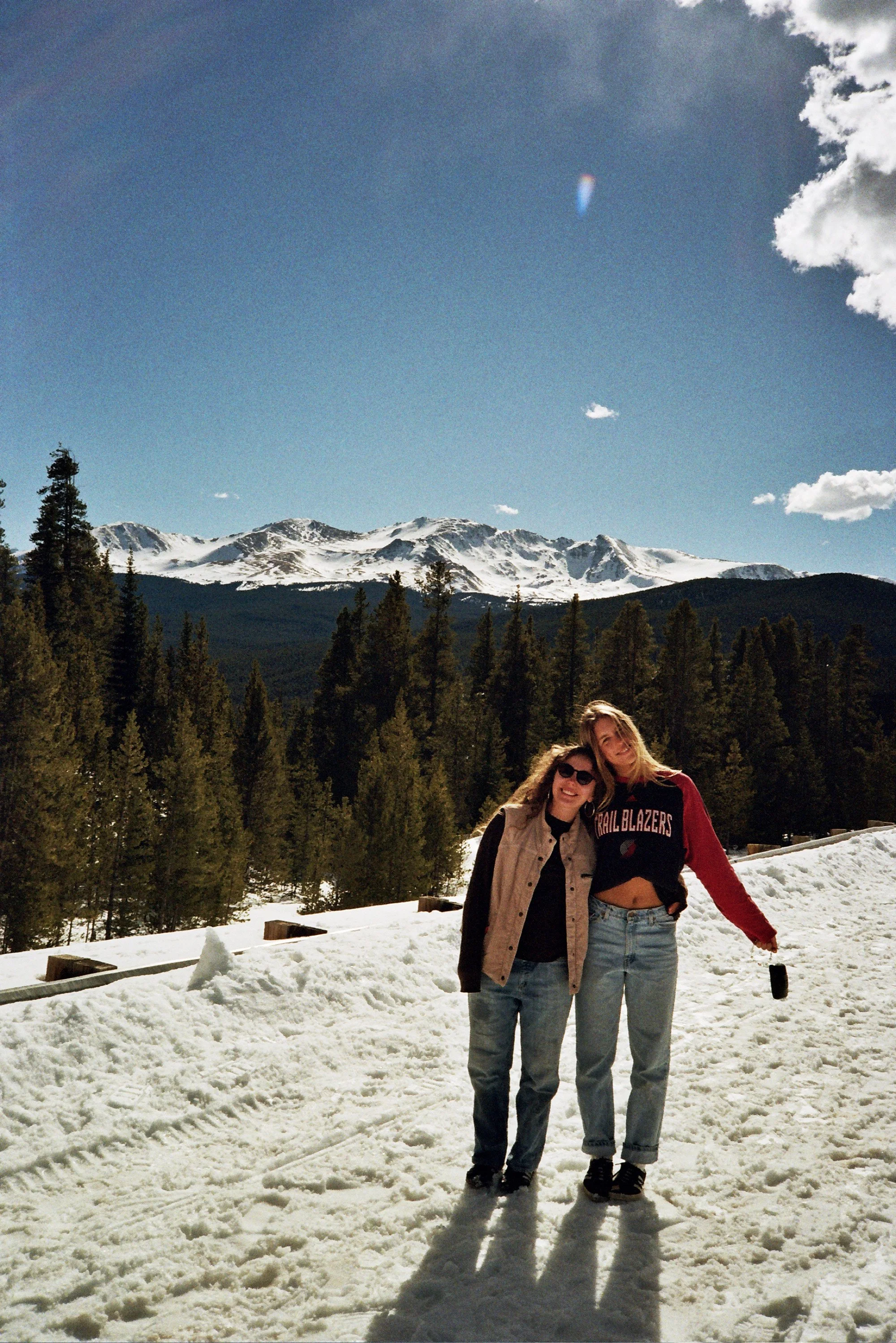 Two women standing together in a snowy landscape with forested mountains in the background, smiling and posing for the photo.