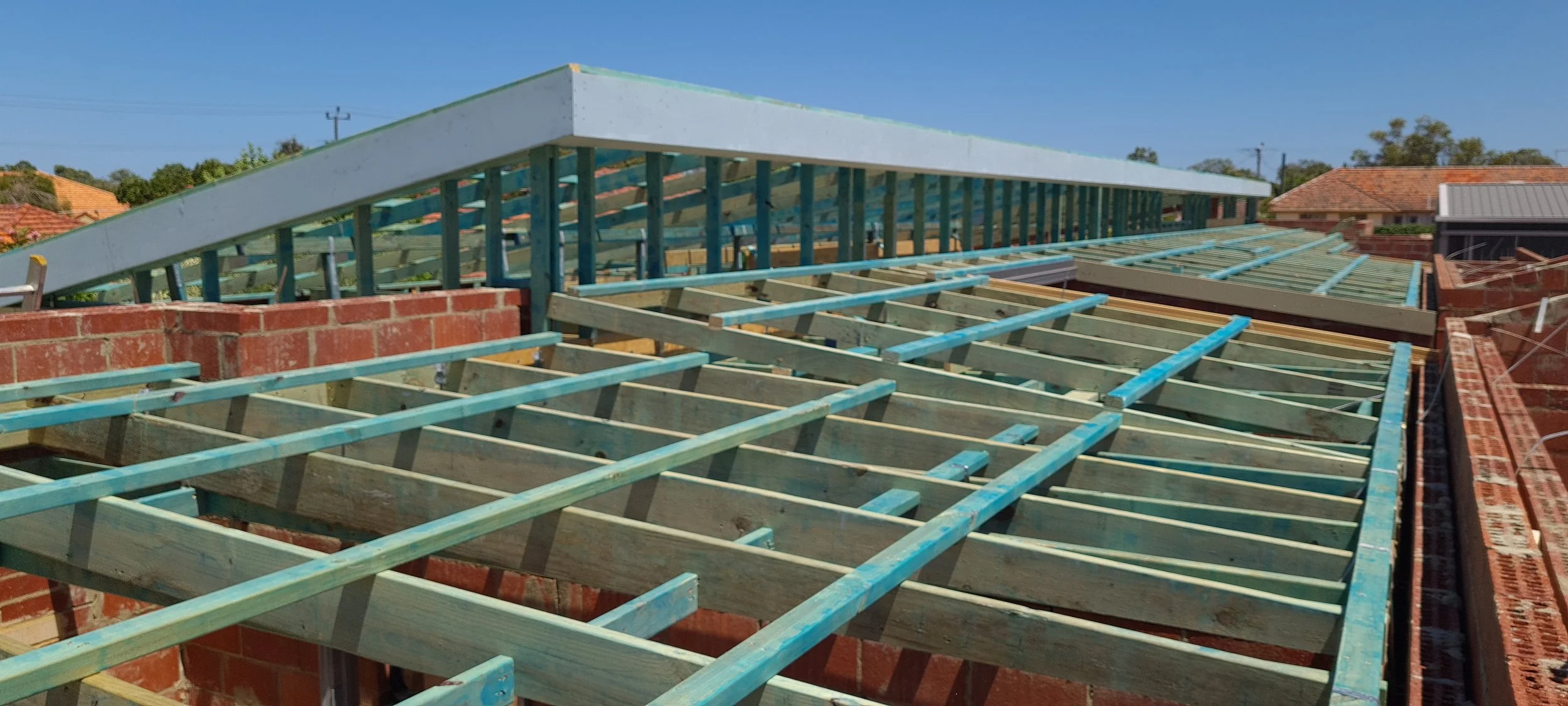 Roof under construction with wooden framing and a partially built roof with a clear blue sky.