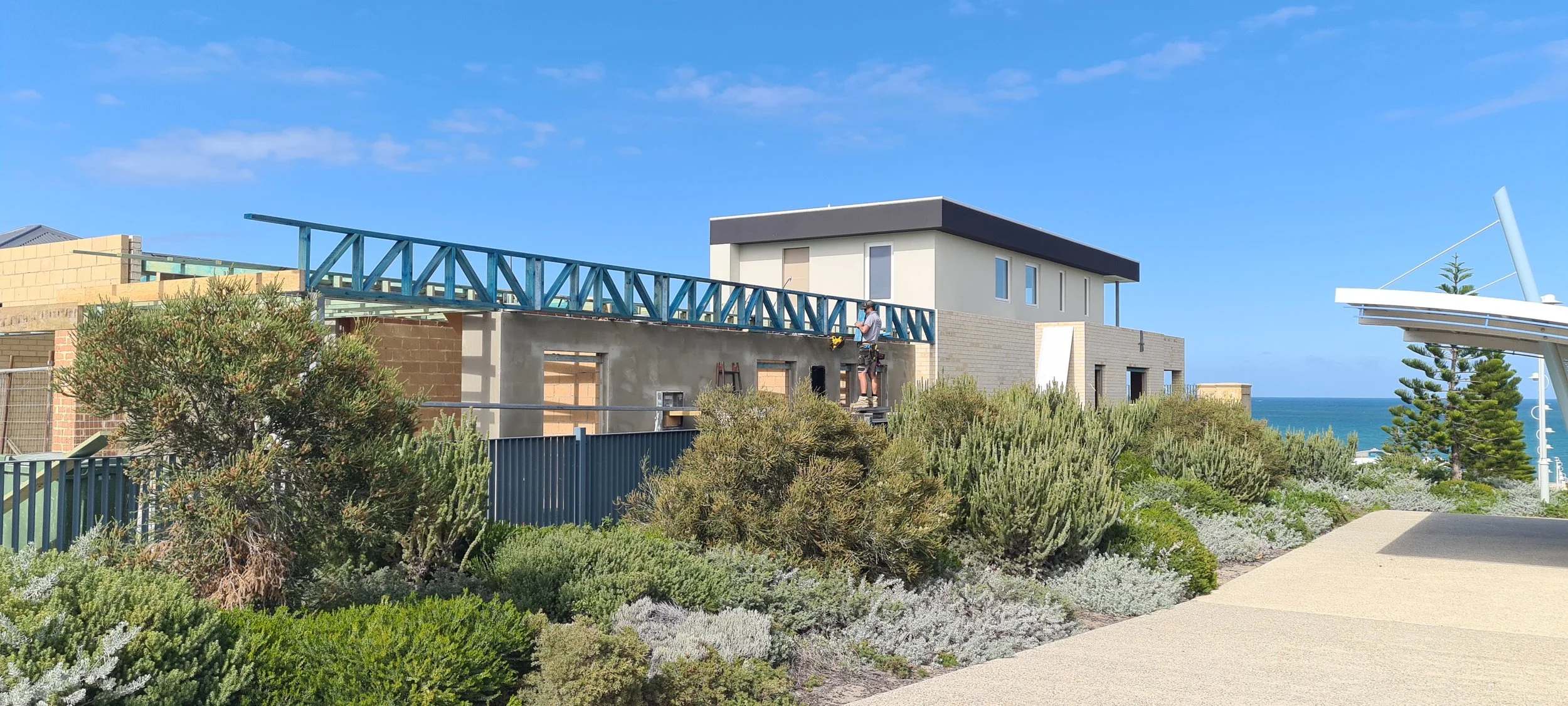 Construction workers building a modern house near the ocean with a clear blue sky.