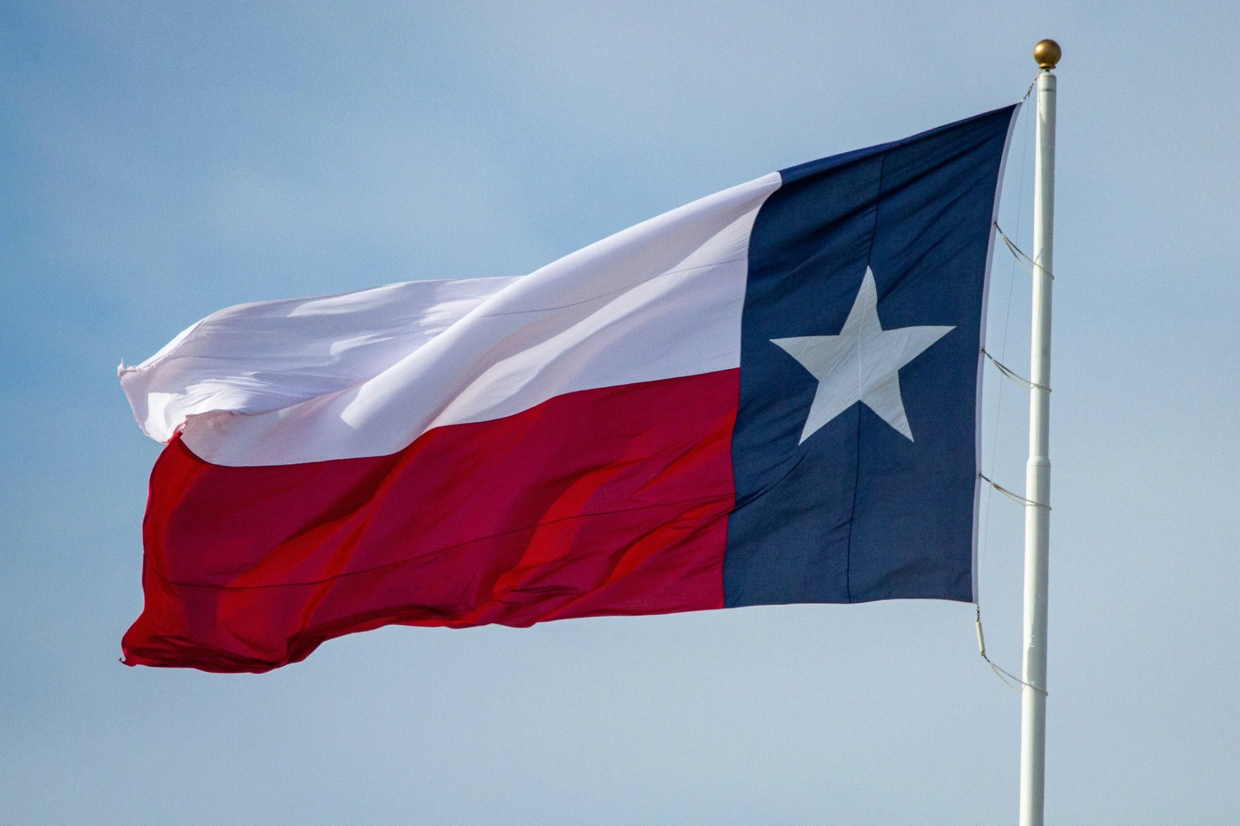 Texas state flag waving in the wind against a clear blue sky.