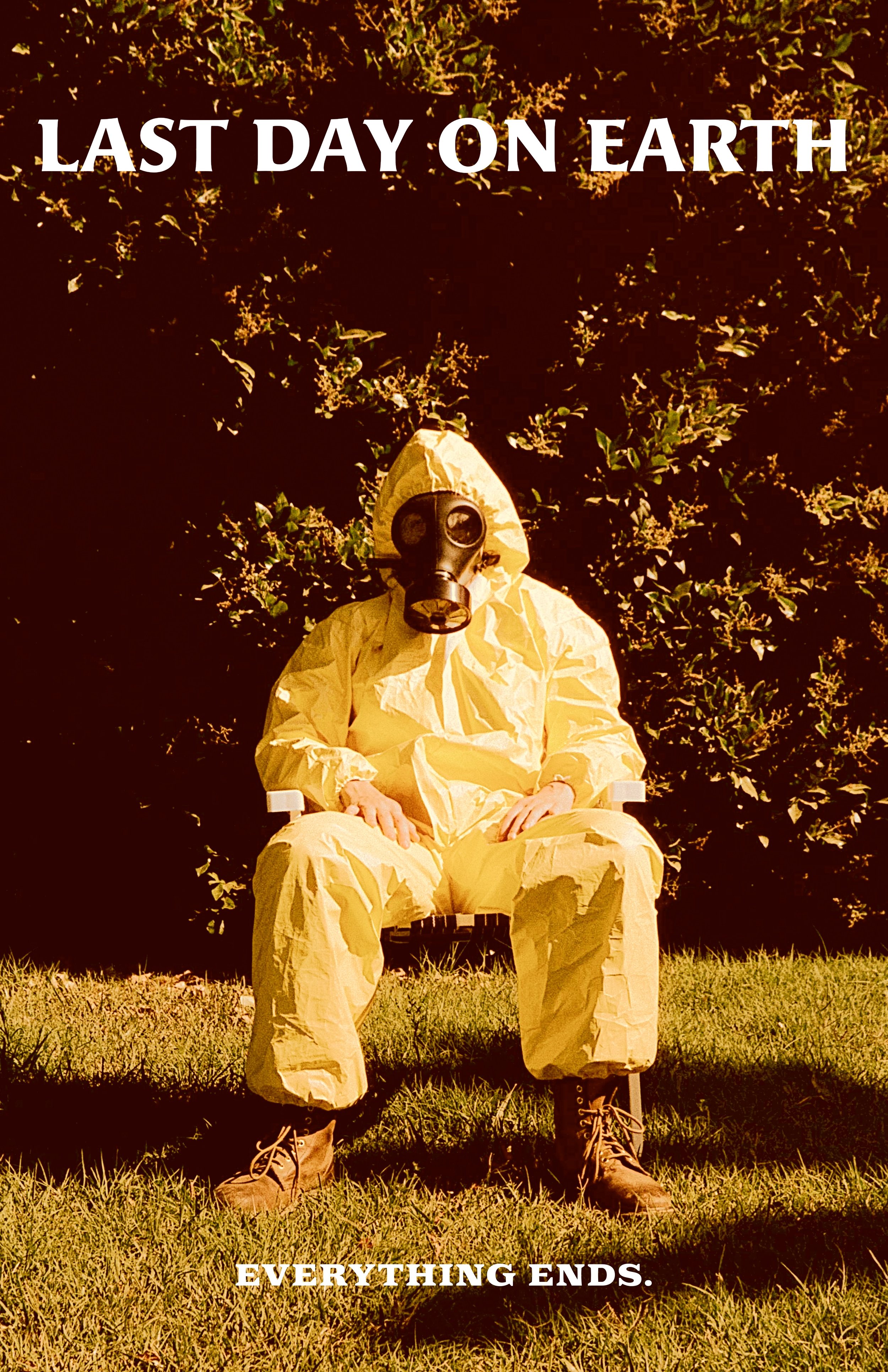 Person in yellow hazmat suit and gas mask sitting outdoors on a grass field with bushes in the background, text at the top says 'Last Day on Earth' and at the bottom says 'Everything Ends'.
