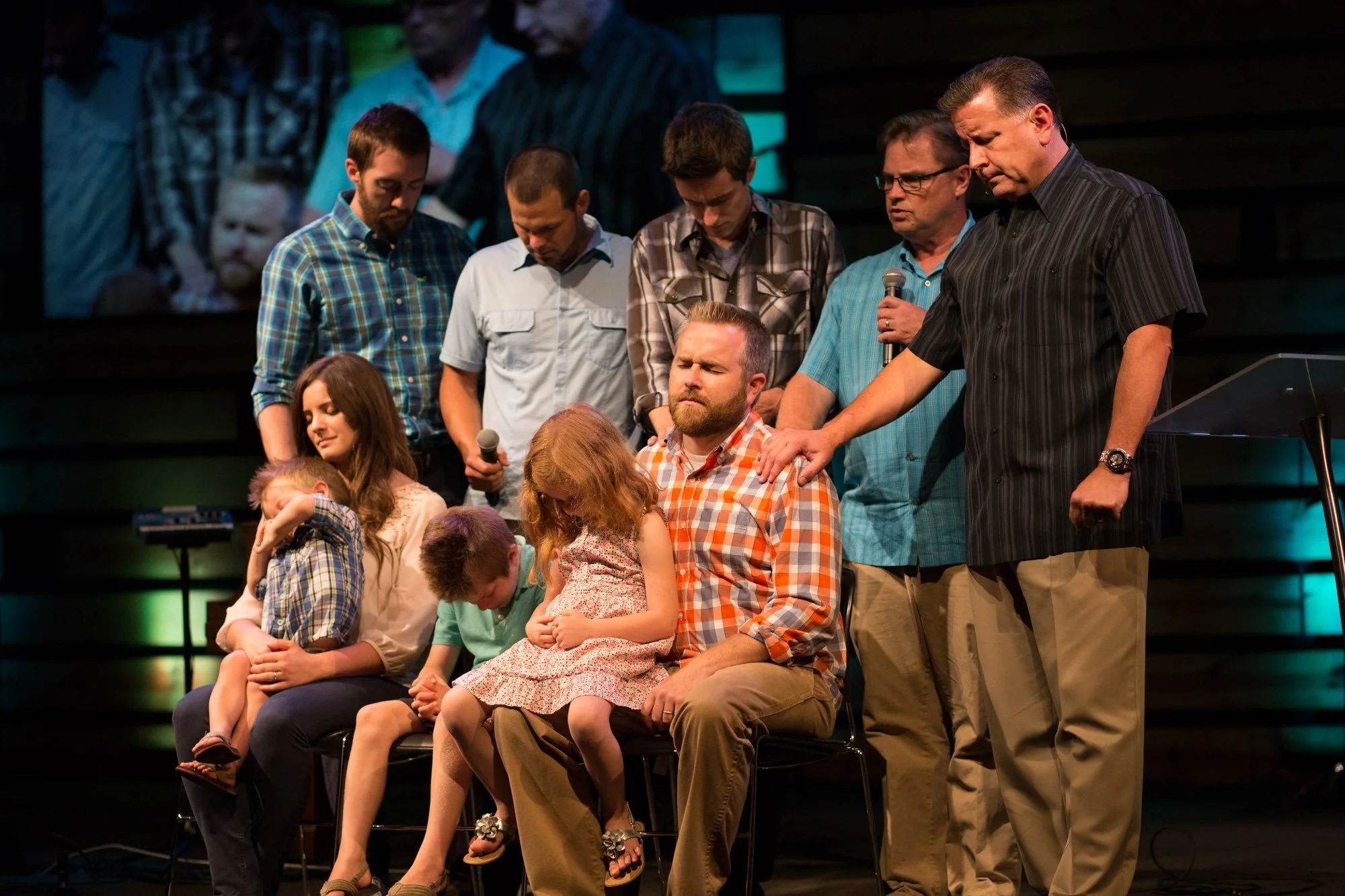 A group of people praying or mourning, with some kneeling and some standing, in a church or auditorium setting.
