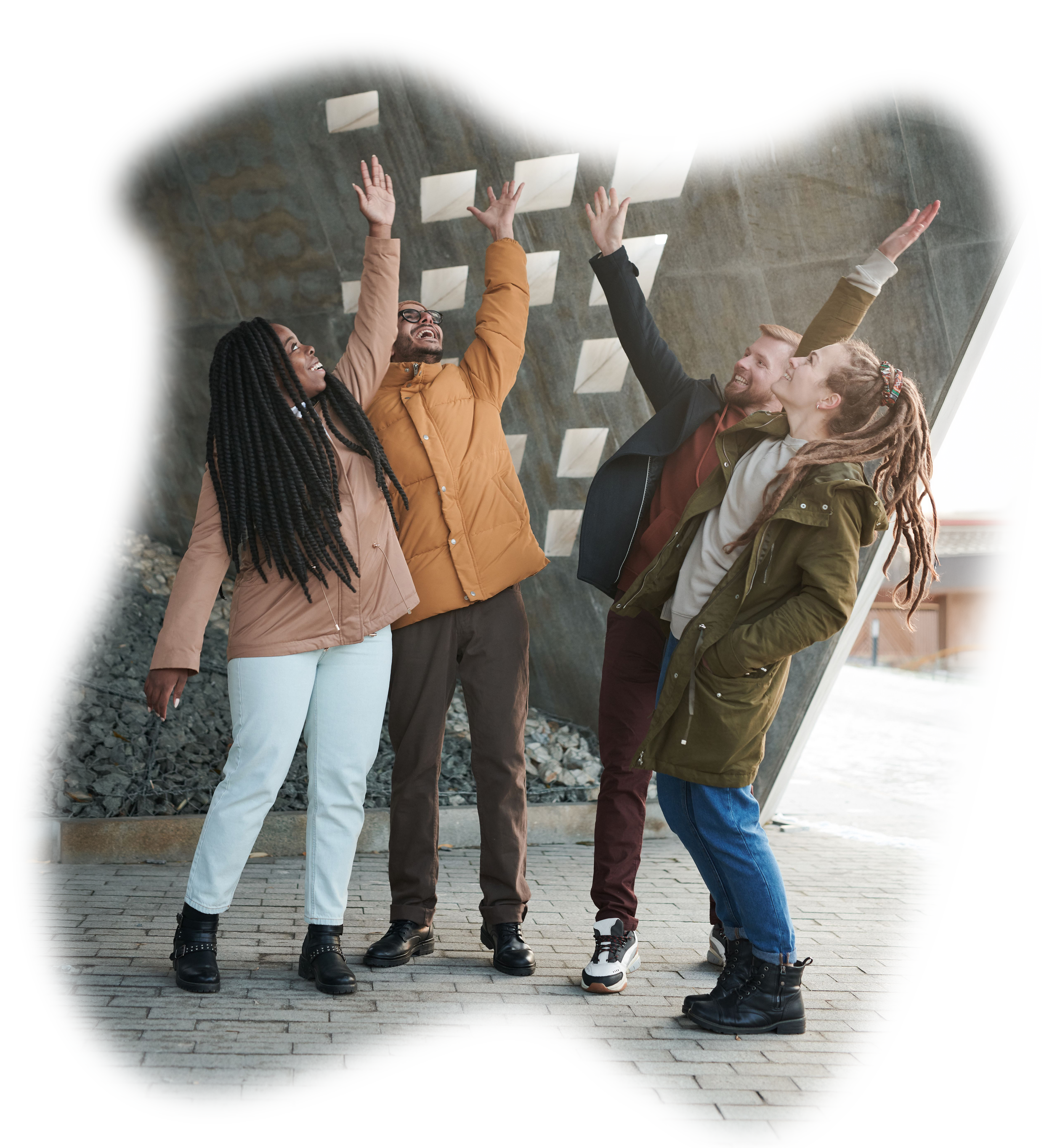Four diverse young adults standing outdoors under a modern concrete structure, smiling, raising hands, and enjoying each other's company.