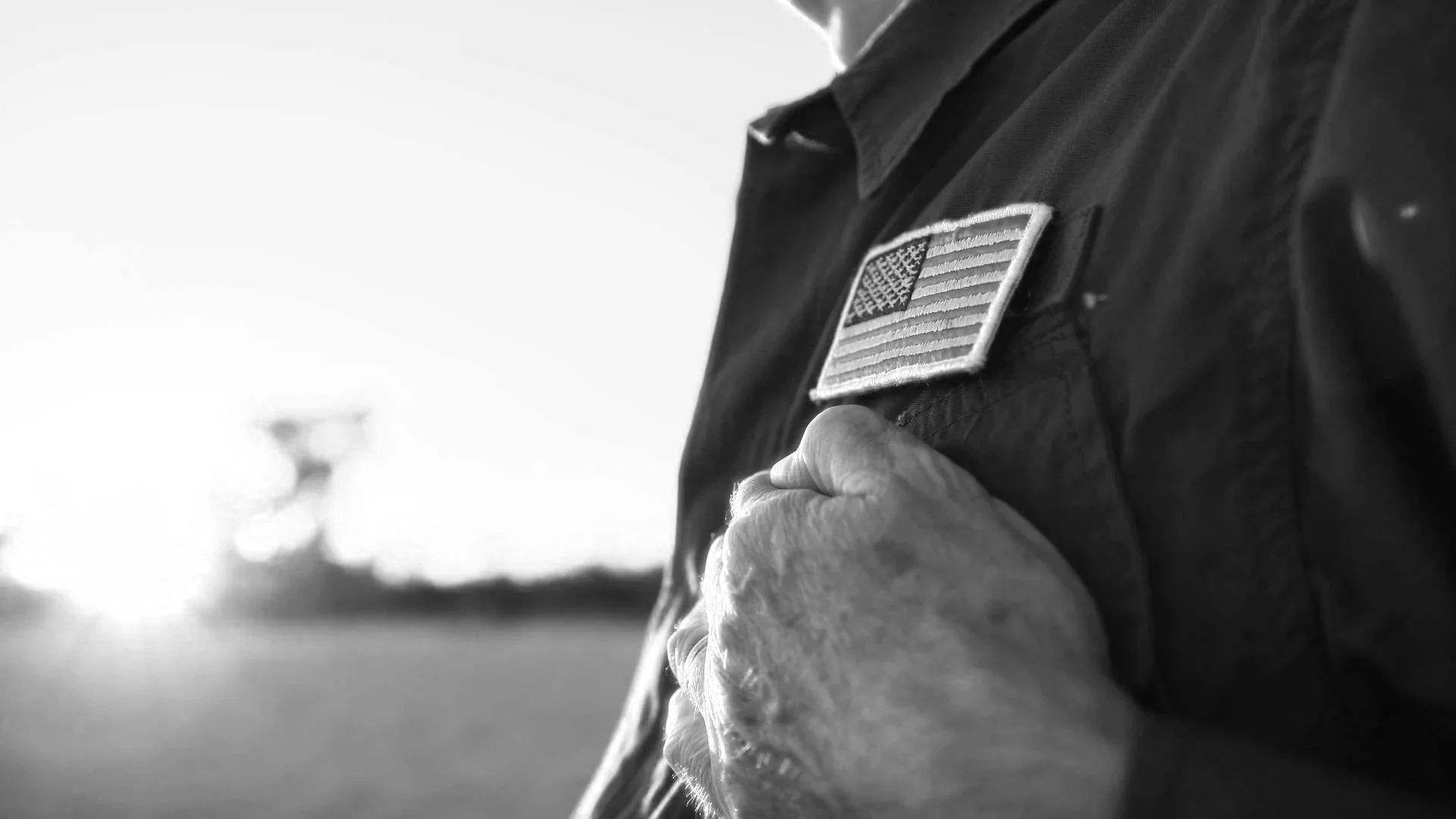 Close-up of a person in a military uniform with an American flag patch, placing their hand over their heart.