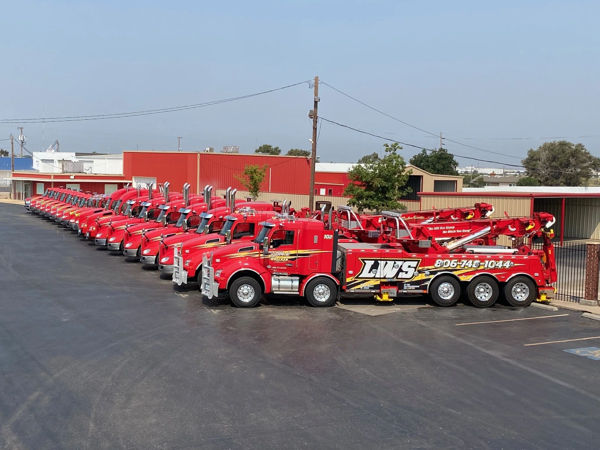 Row of red fire trucks parked in an outdoor lot near a beige and red building with a red roof.