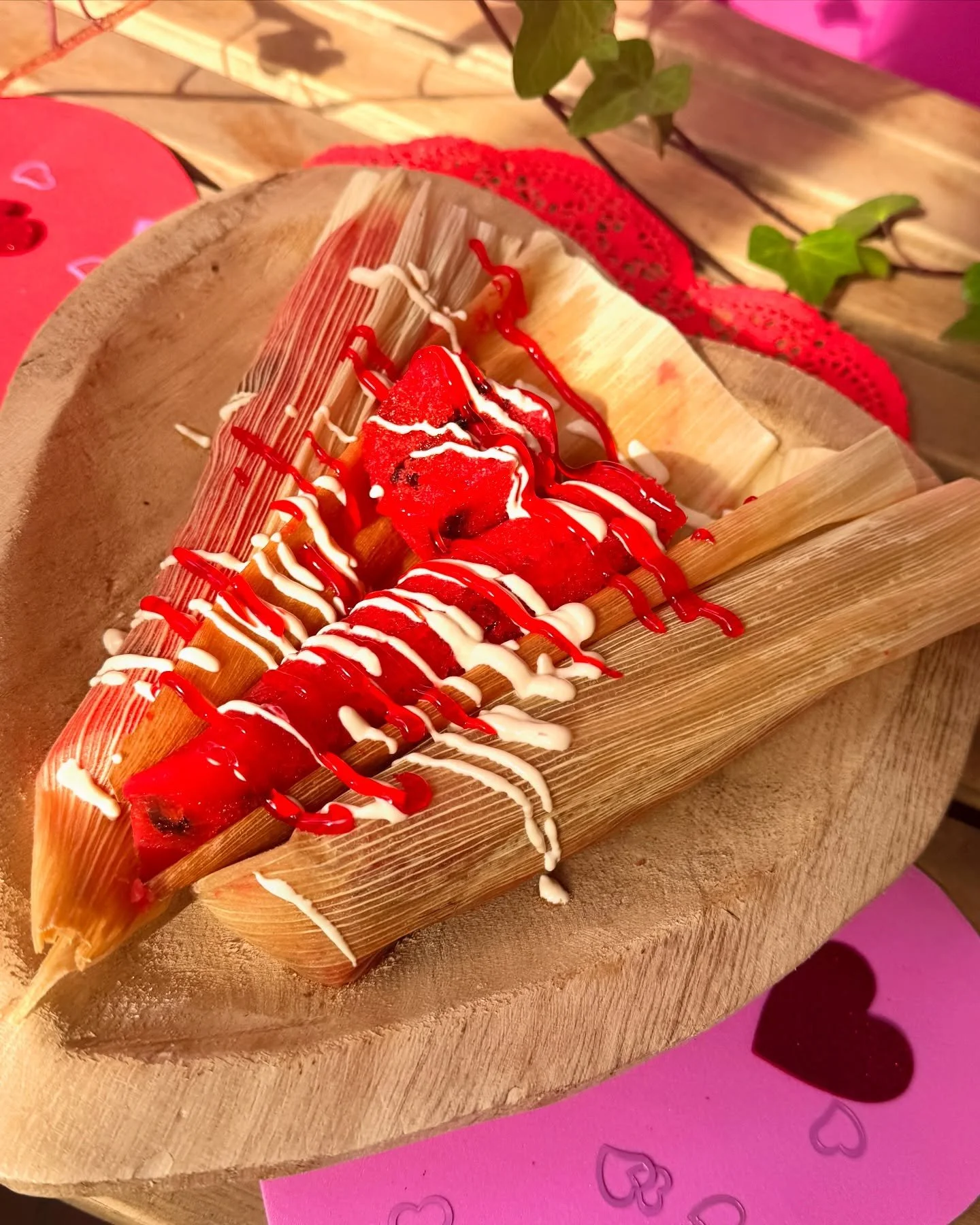 Sweet treat with strawberries, white and red chocolate drizzle served on bamboo leaf on a wooden round tray with pink and red heart-embossed paper underneath.