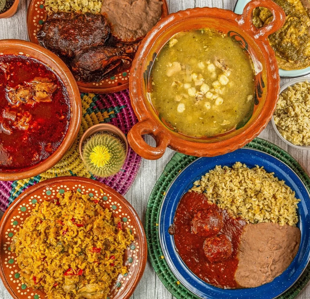 Assorted traditional Mexican dishes including rice, salsas, and stews served in colorful ceramic bowls on a wooden table.