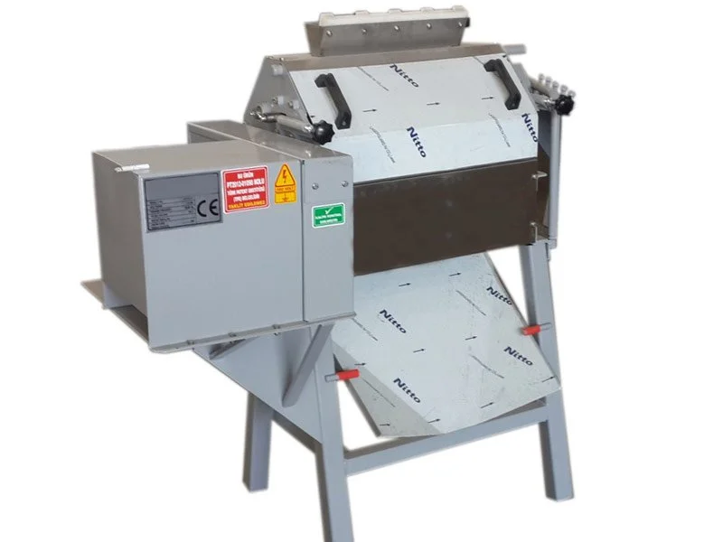 A stainless steel industrial machine with warning labels, a sliding cover, and a stand base, used for food processing or manufacturing.