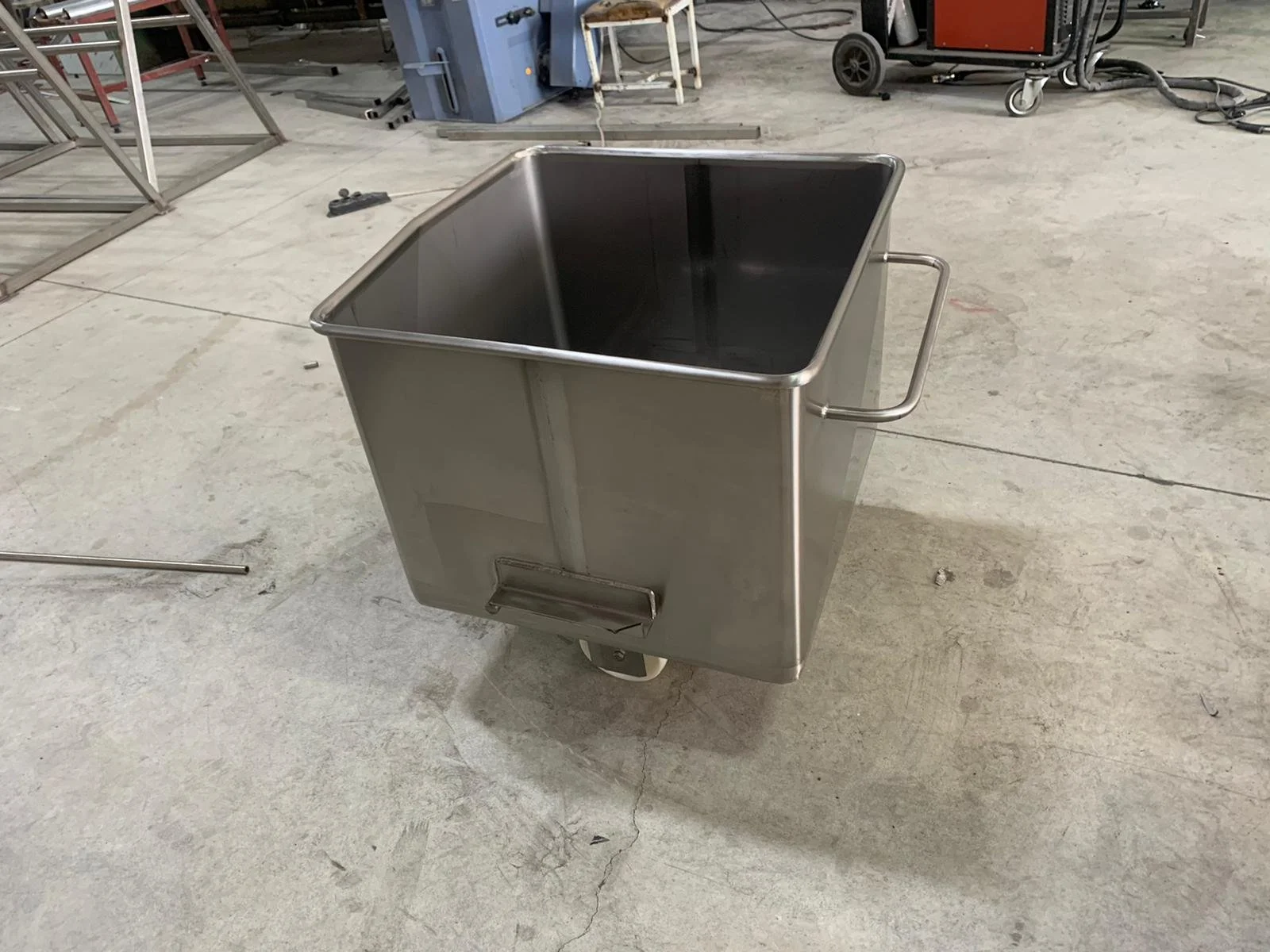 Stainless steel utility cart with handles on each side, placed on a concrete workshop floor. The cart is empty and appears to be in a workshop setting.