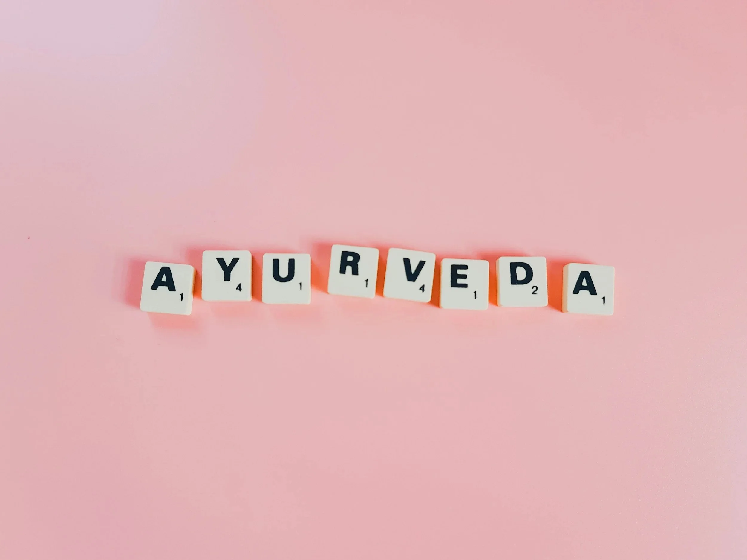 pink background, letter tiles that spell out A-Y-U-R-V-E-D-A : Ayurveda
