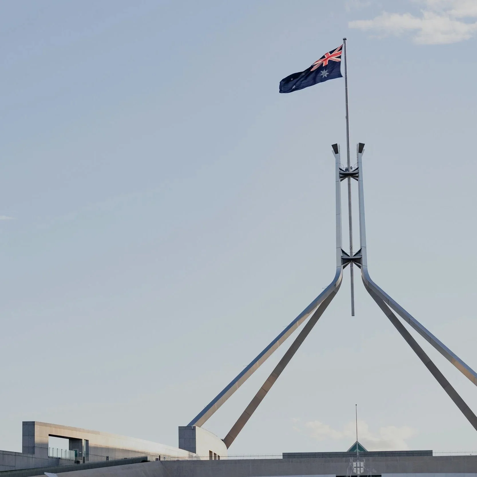 Australian Parliament House with its flag flying on a pole against a cloudy sky.
